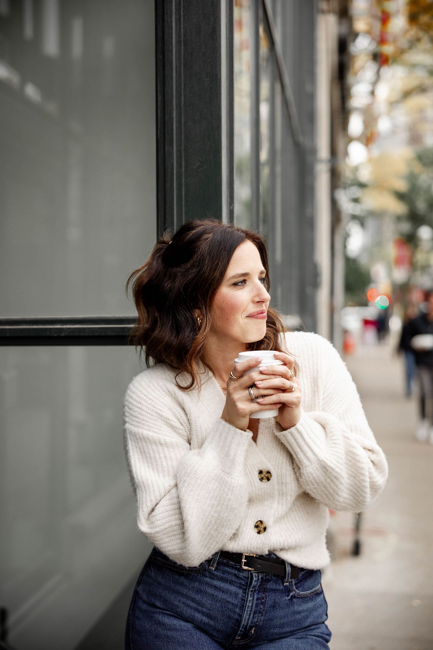 Person in white sweater leaning against storefront window in urban setting.
