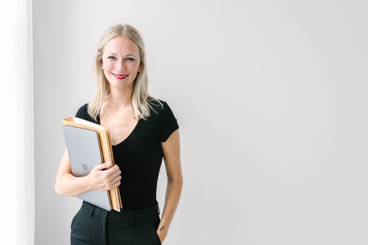 Professional in black attire holding folders against white wall.
