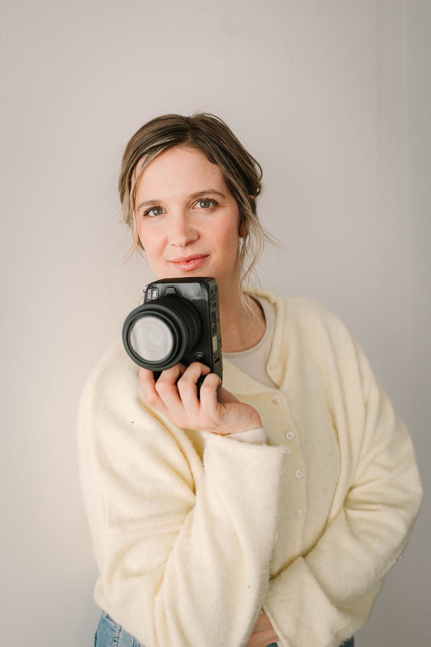Creative self-portrait series with camera in cream sweater against neutral backdrop.