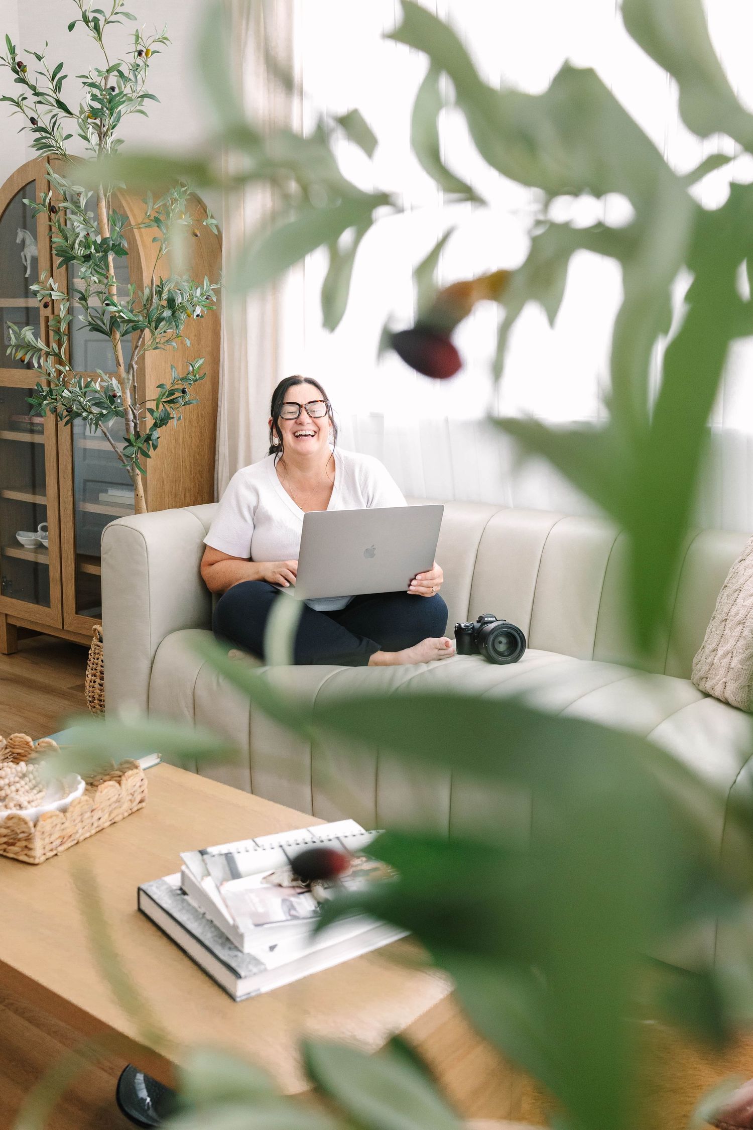 A person relaxes on a white couch reading while surrounded by green houseplants in a bright, modern living room.