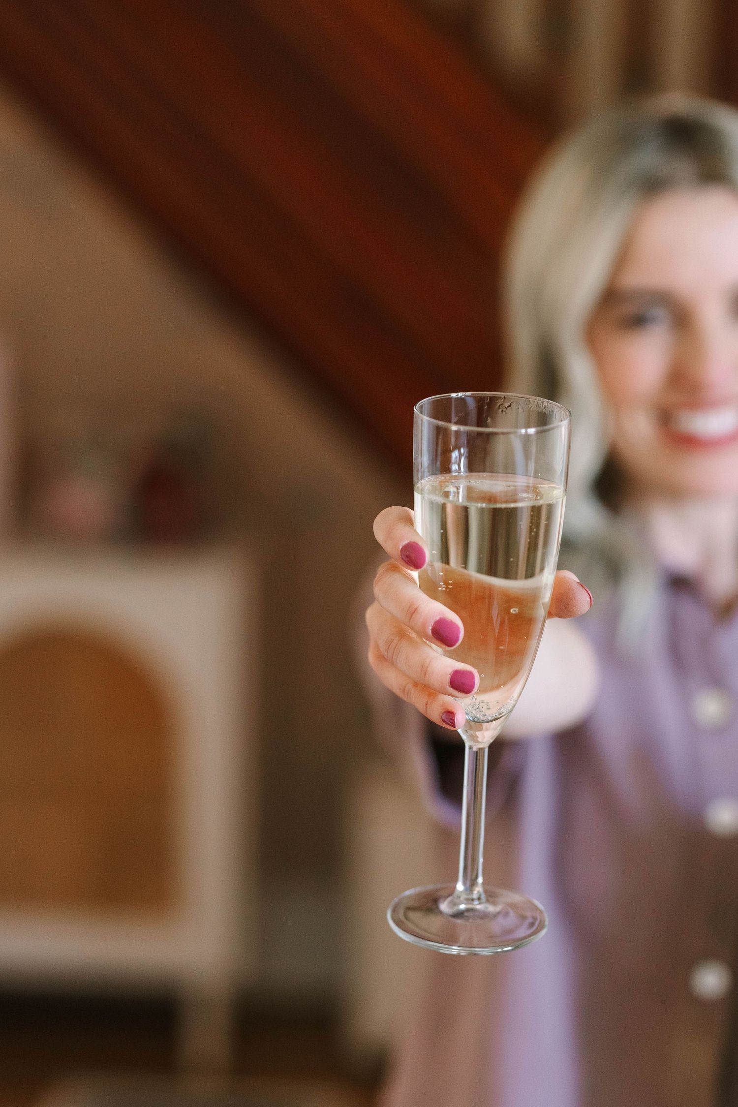Hand holding up a glass of rosé wine against a warm wooden background.