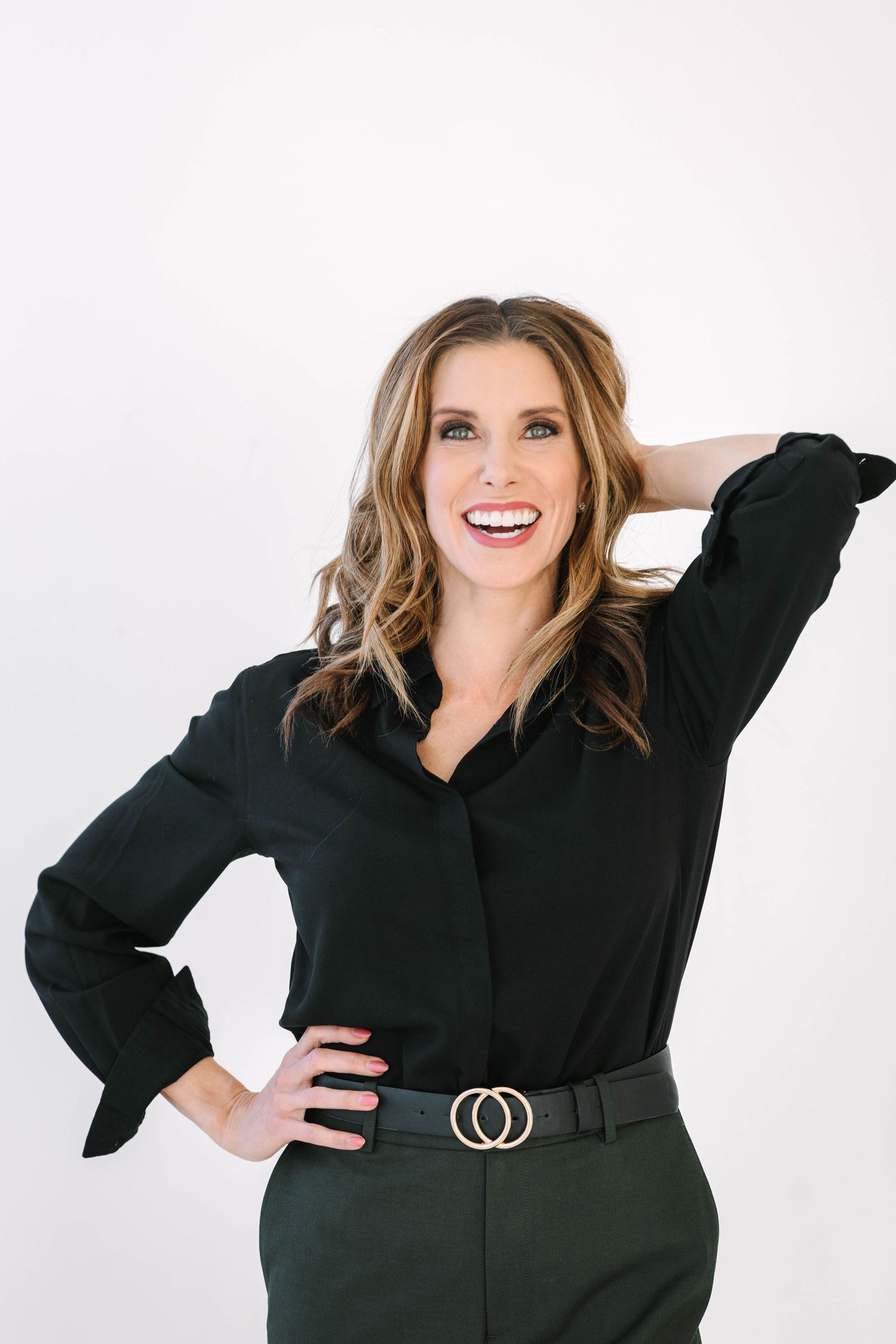 Professional portrait of someone wearing a black blouse and green pants with a double ring belt against white background.