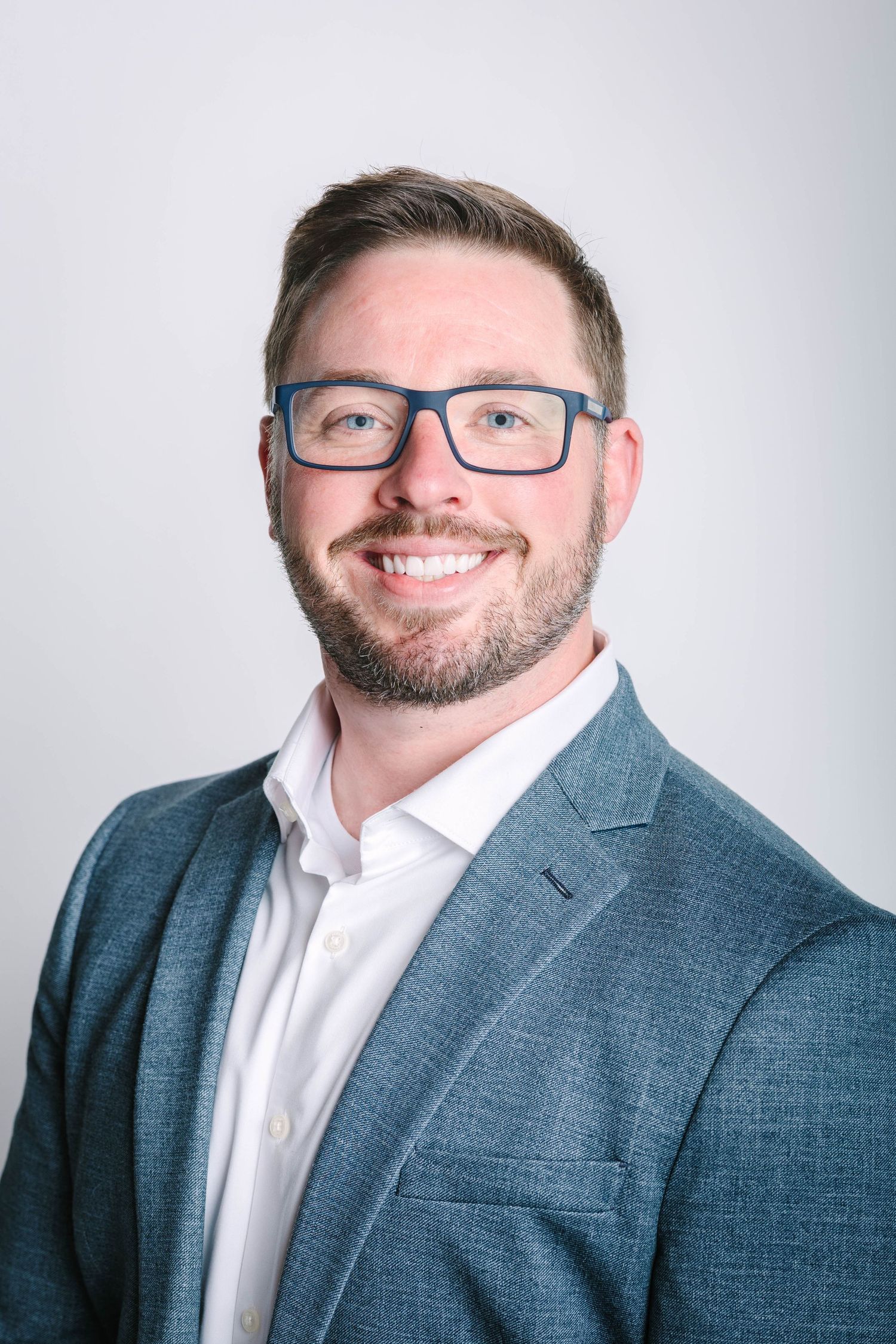 Professional headshots of person in blue blazer and glasses against light background.