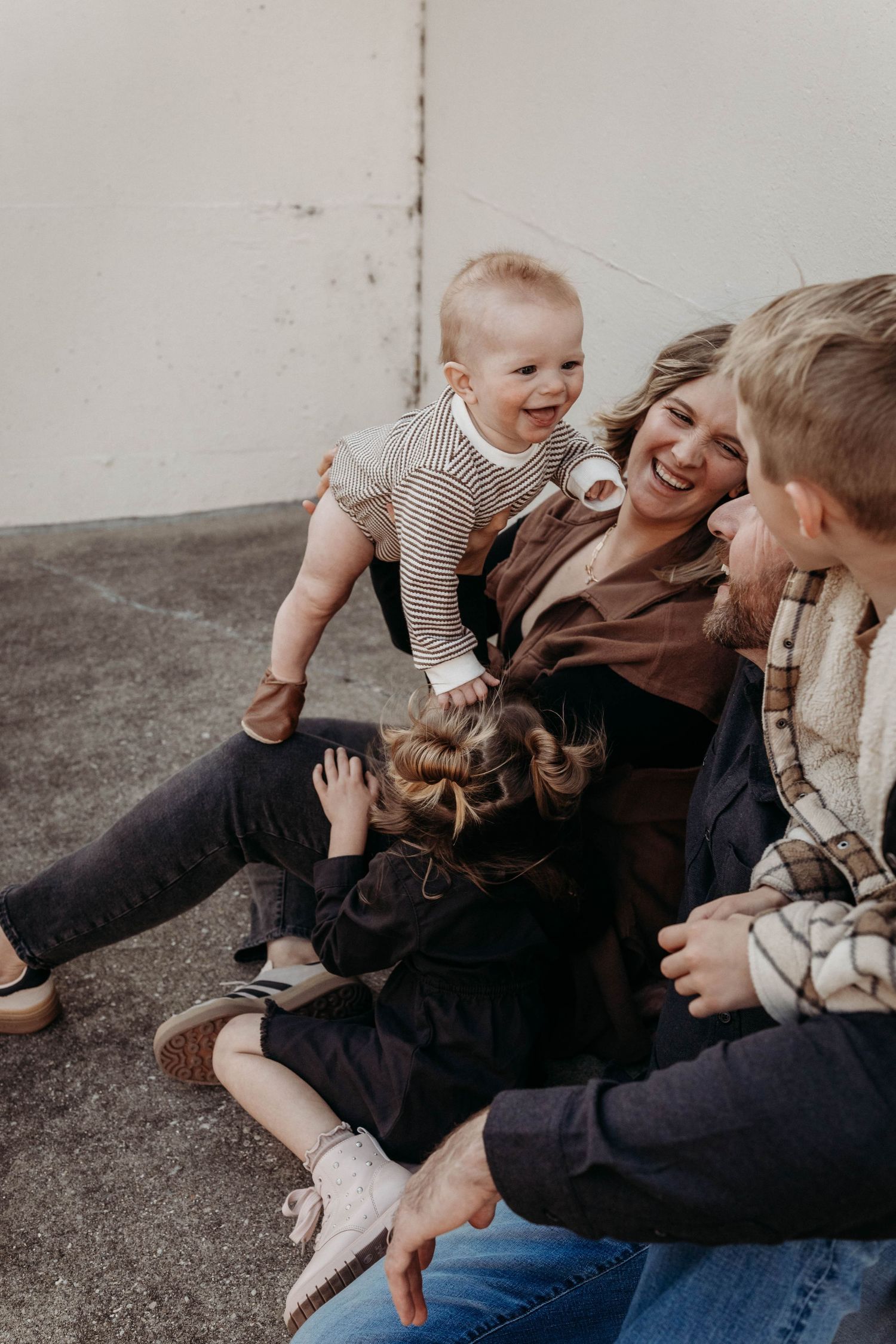 Family lying together on grey floor sharing joyful candid moments.
