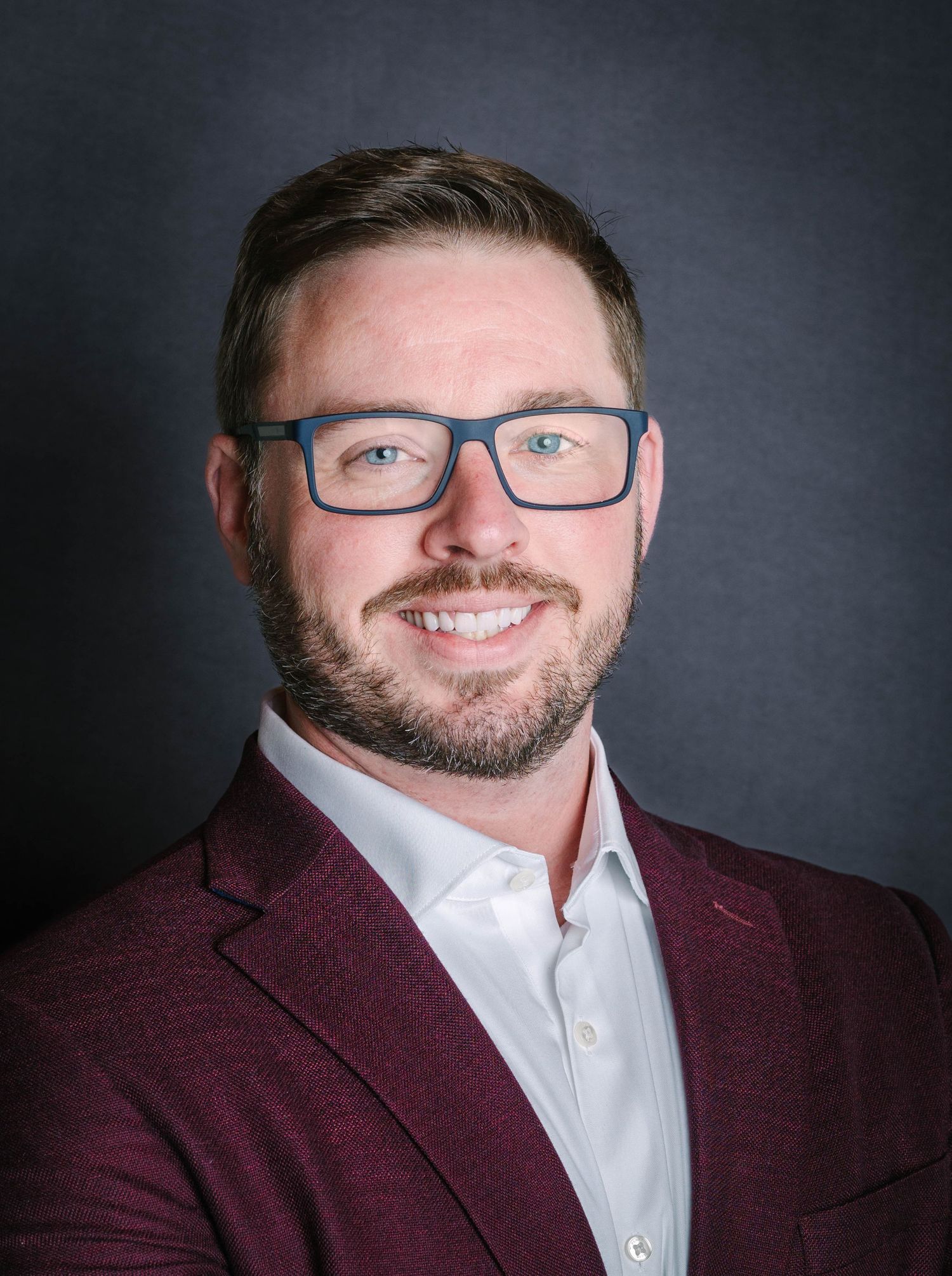 Professional portrait series of person in burgundy blazer and glasses against dark background.