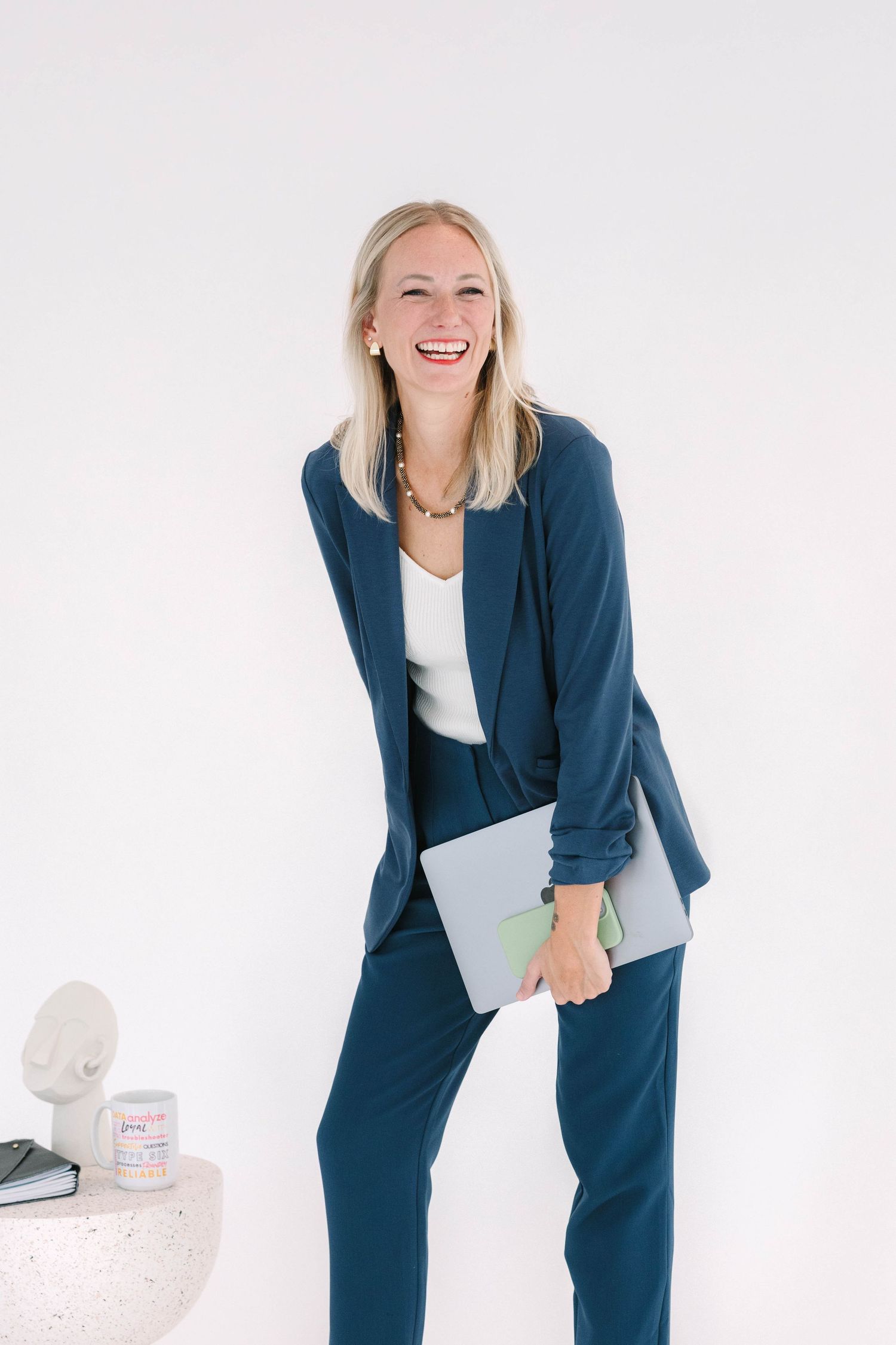 Professional wearing a navy blue blazer and white top holding a laptop against white background.