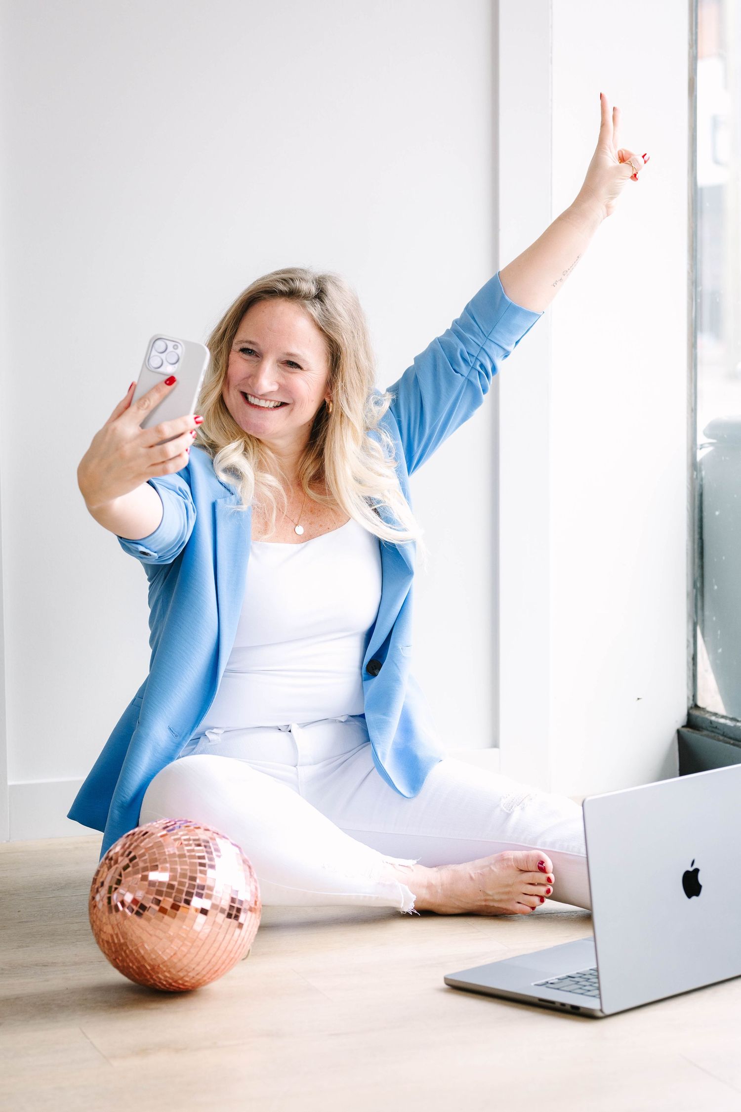 Woman in blue blazer taking selfie with laptop and disco ball in bright room.