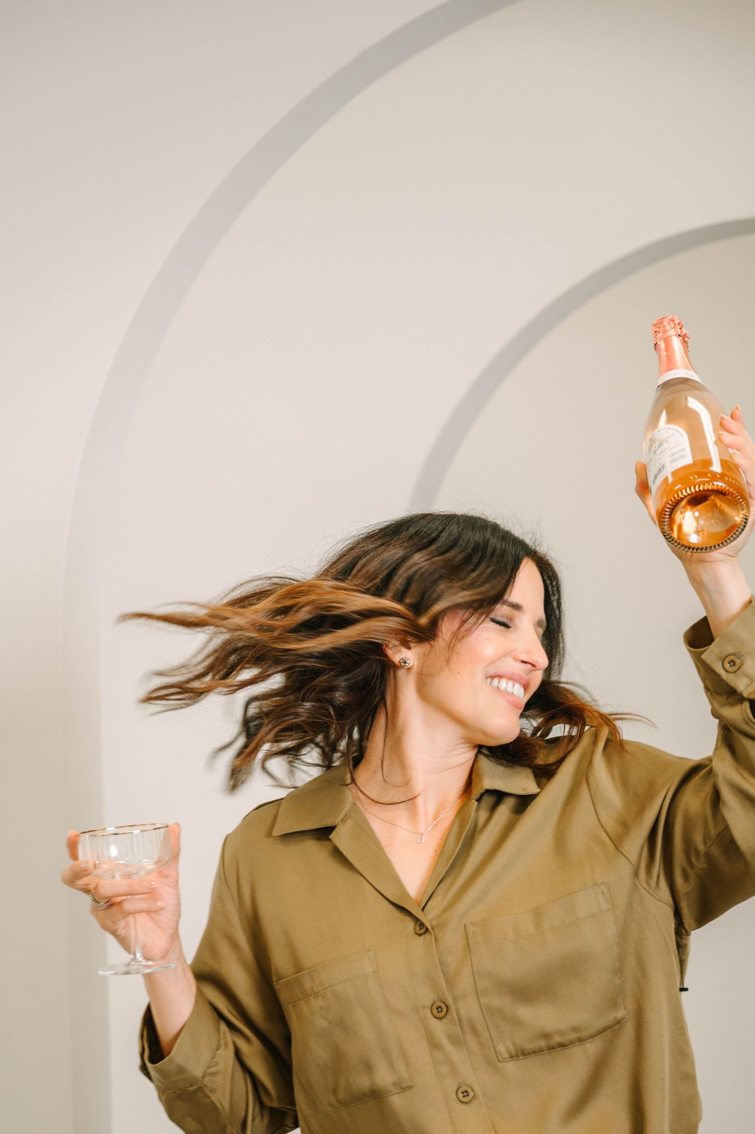 A person in a tan button-up shirt dances joyfully with flowing hair against a light background in a photo sequence.