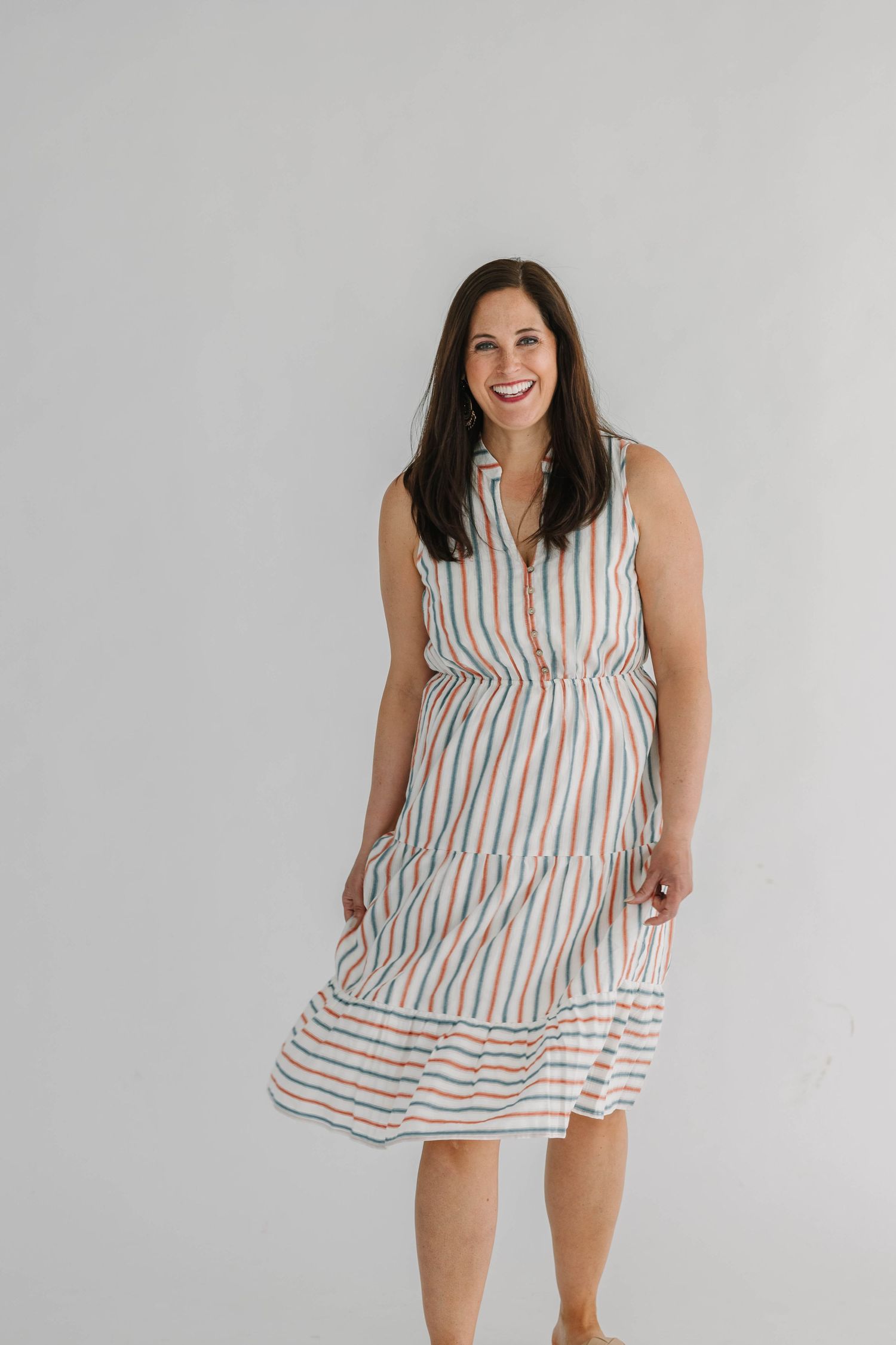 Woman smiling in a sleeveless white striped midi dress with colorful stripes, posing against a light gray background.