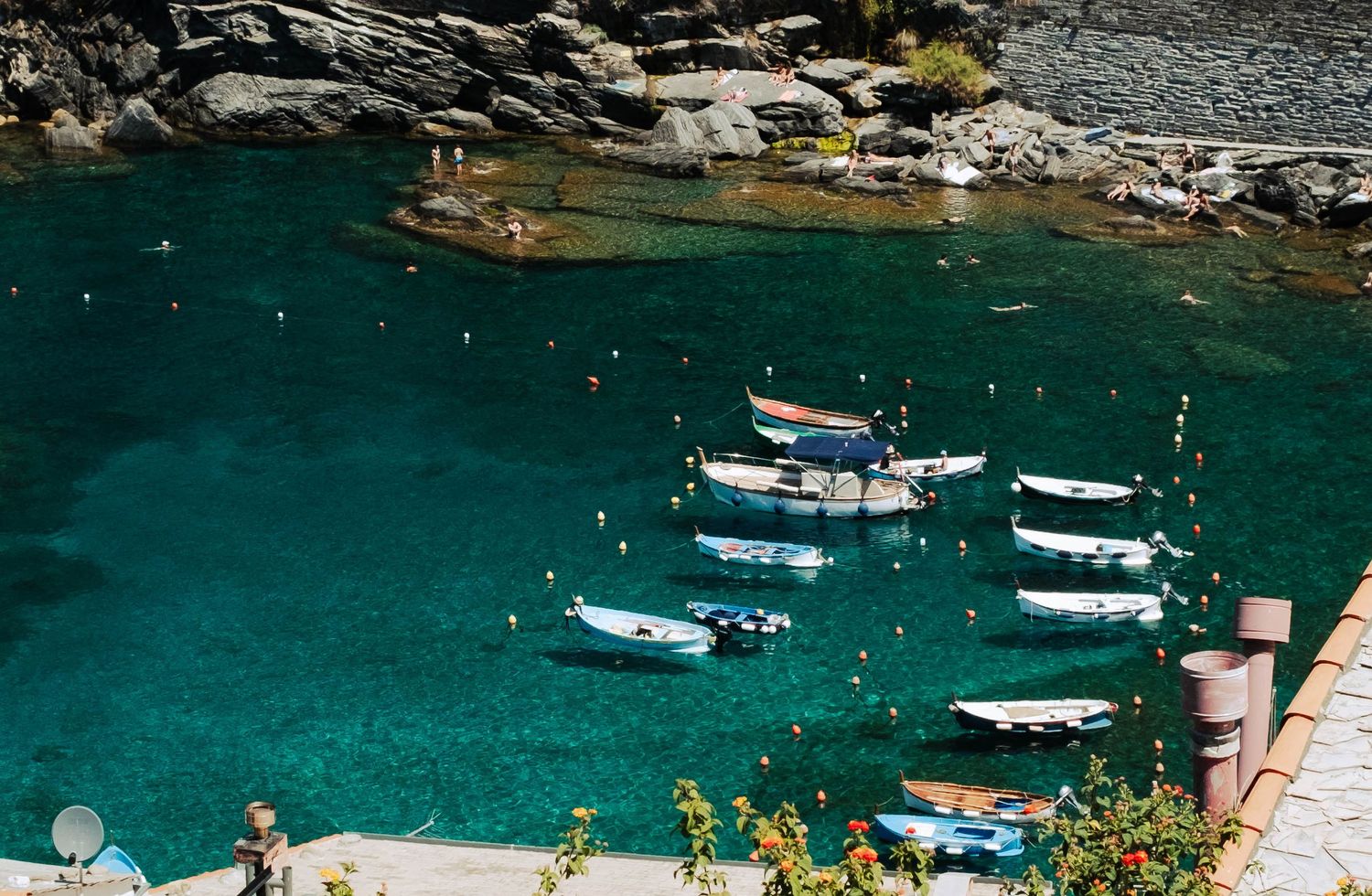 Small wooden boats float in a crystal-clear turquoise harbor surrounded by rocky cliffs and lush greenery.