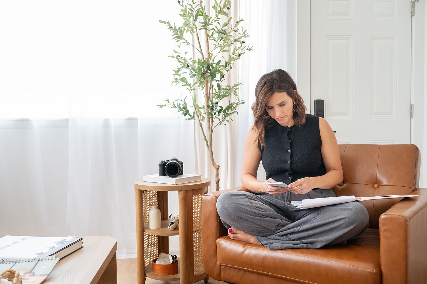 A person sits cross-legged in a brown leather armchair while working on a laptop in a bright, modern room.