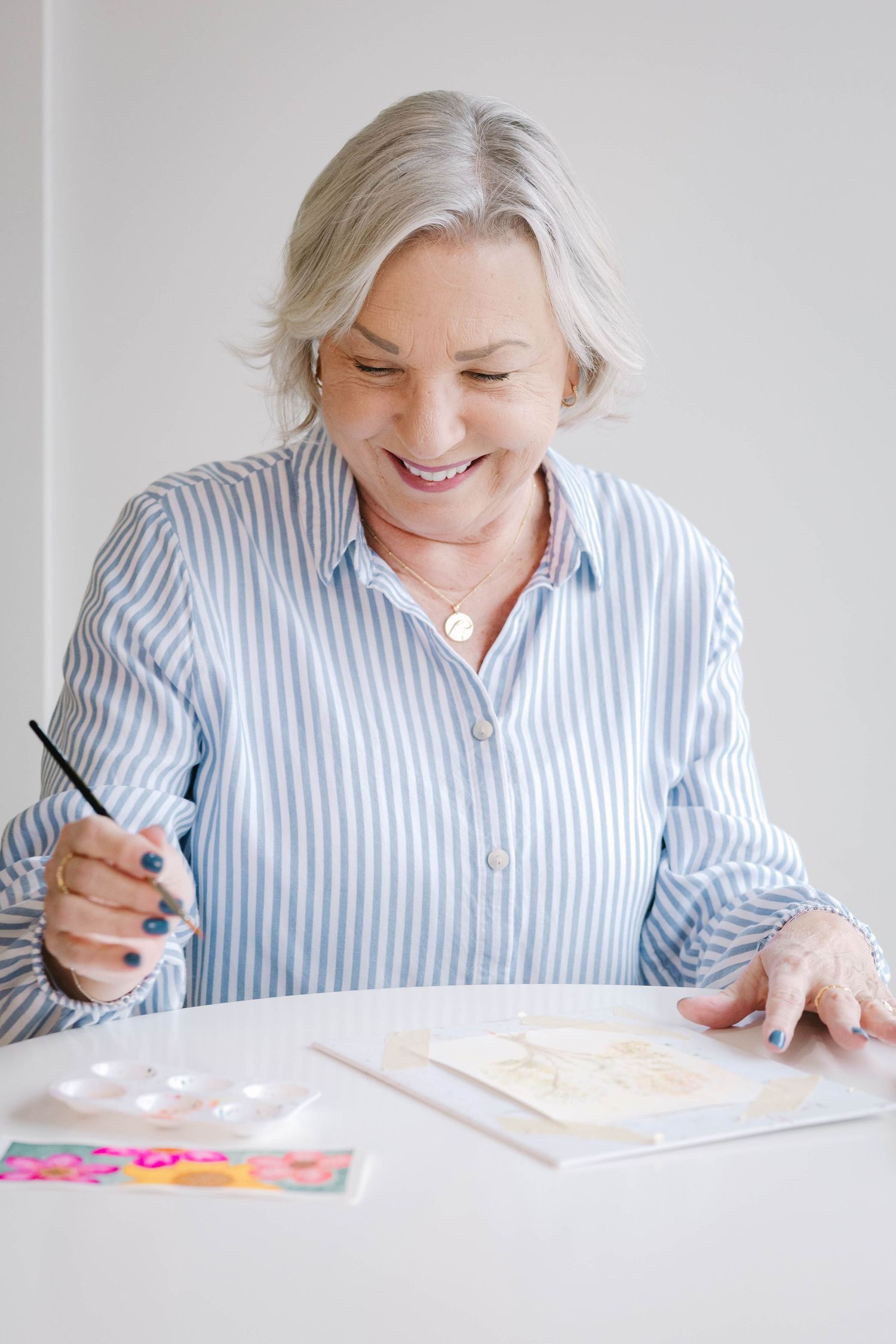 Series of watercolor painting moments in striped blue shirt at white desk.