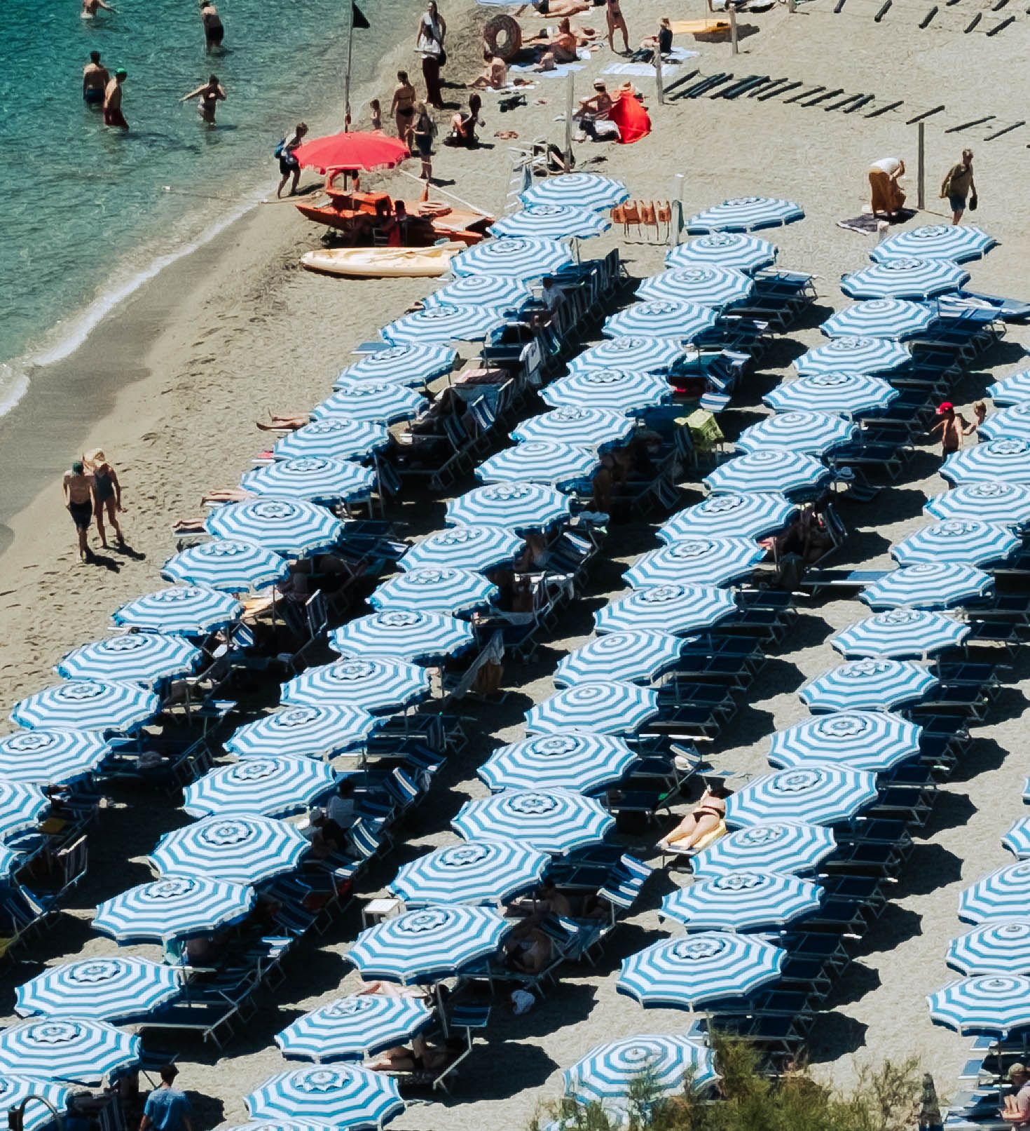 Aerial view of rows of blue and white striped beach umbrellas on a crowded sandy beach.