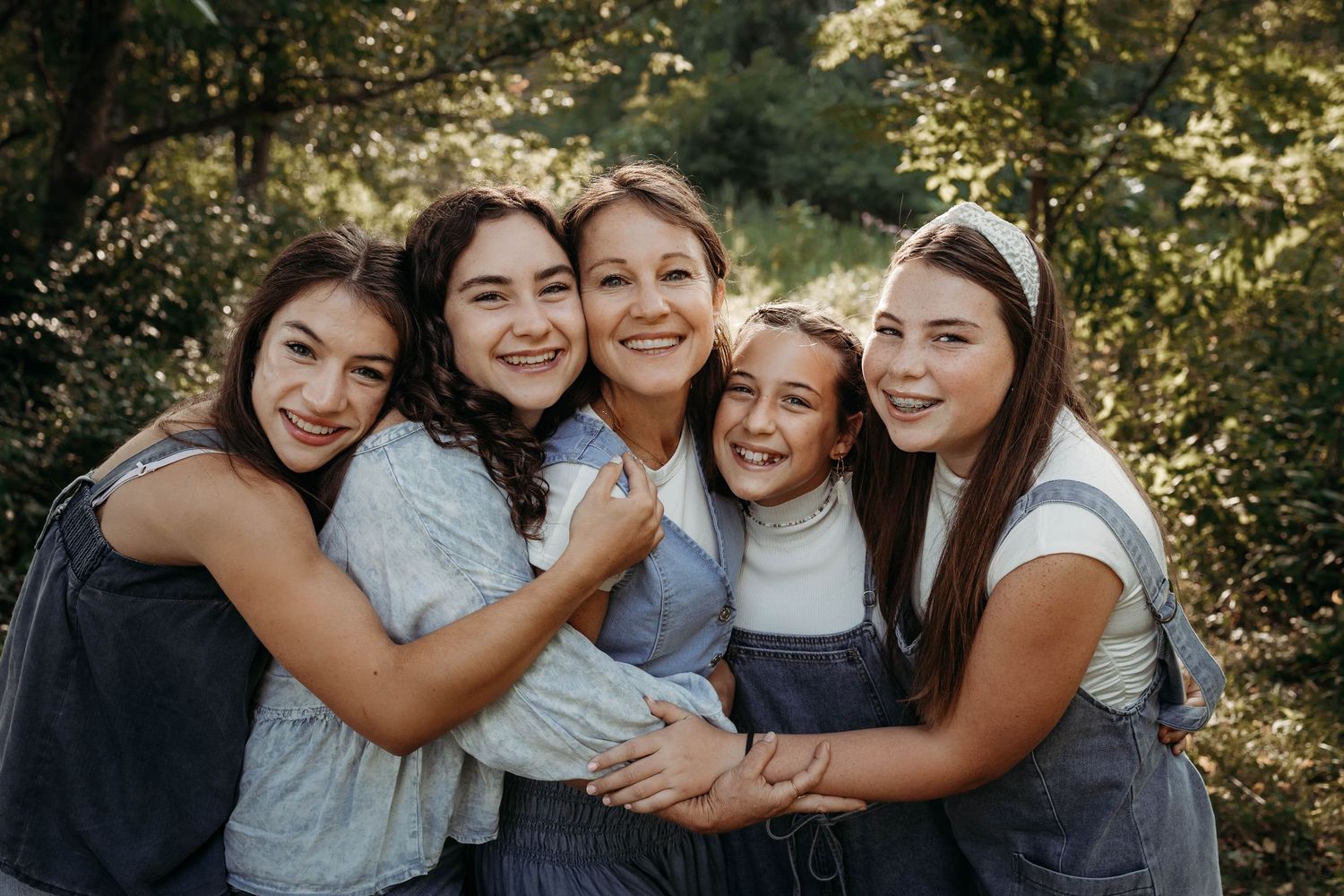 Group of friends laughing and hugging together outdoors in natural sunlight.