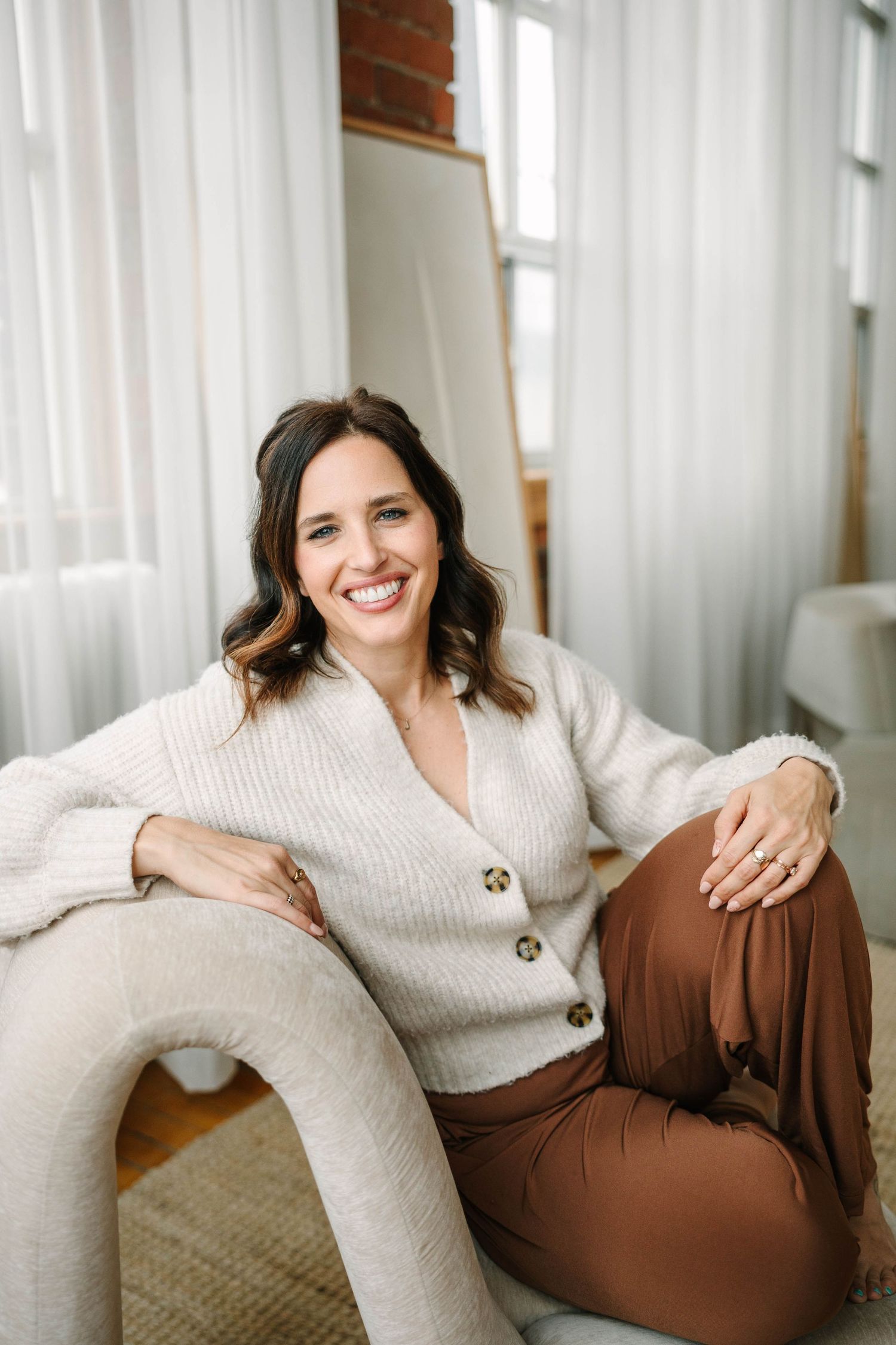 Four lifestyle photos showing a person in a cream sweater and brown pants relaxing on a couch by a window.