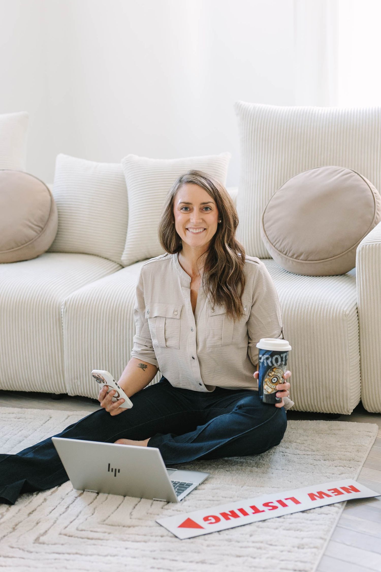Casual home office setup with laptop and soda can on cream carpet next to white couch with decorative pillows.
