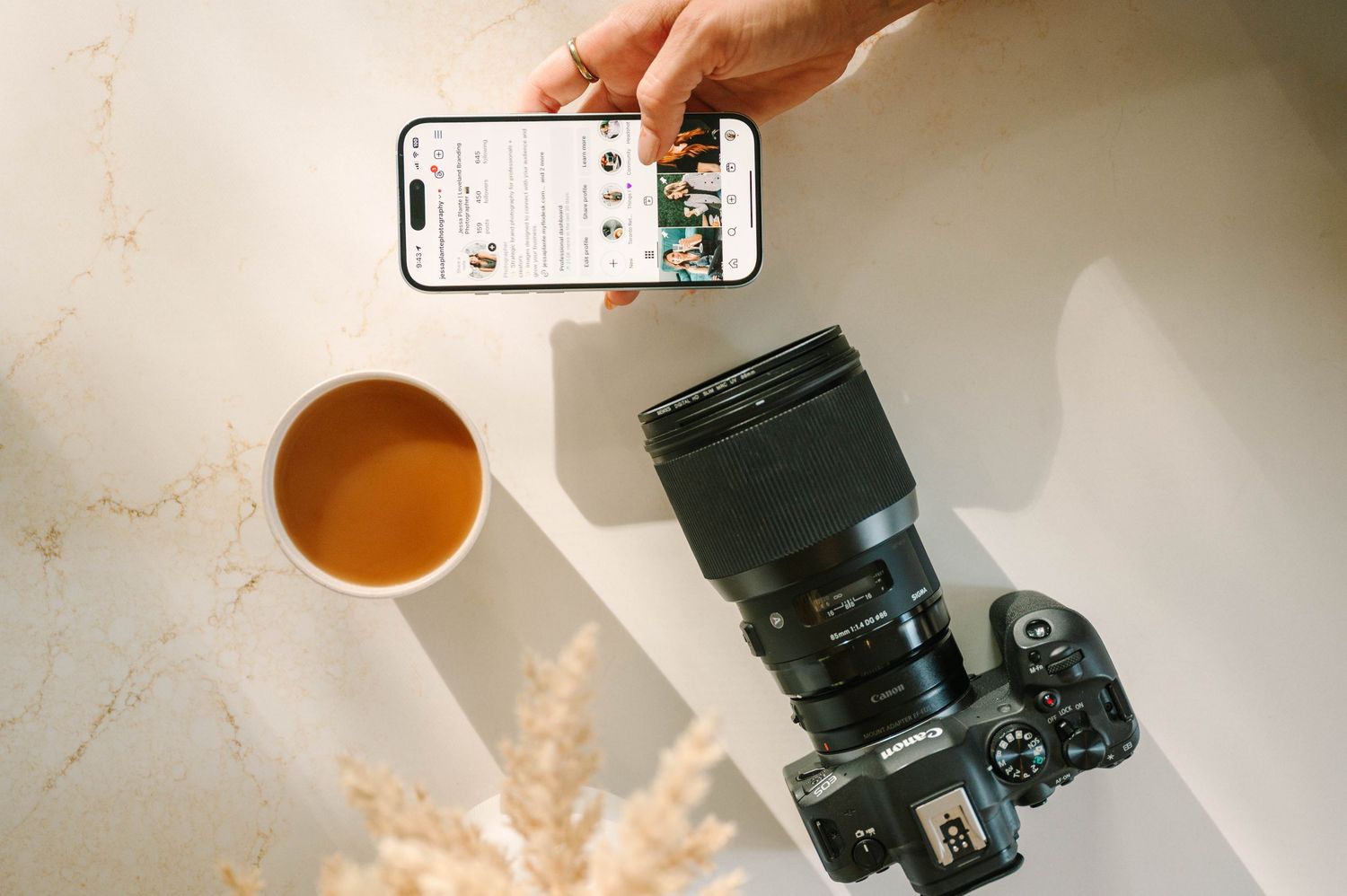 A camera lens sits next to a cup of coffee on a white marble surface with warm lighting.