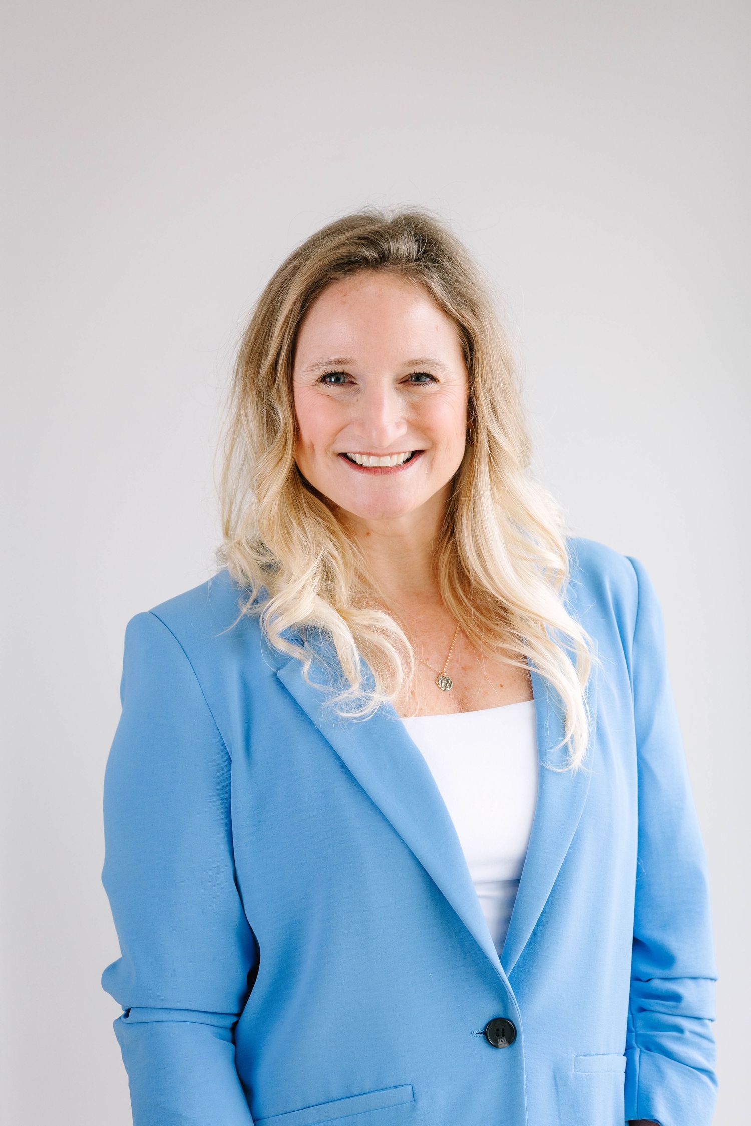 Professional headshot of person in light blue blazer against white background.
