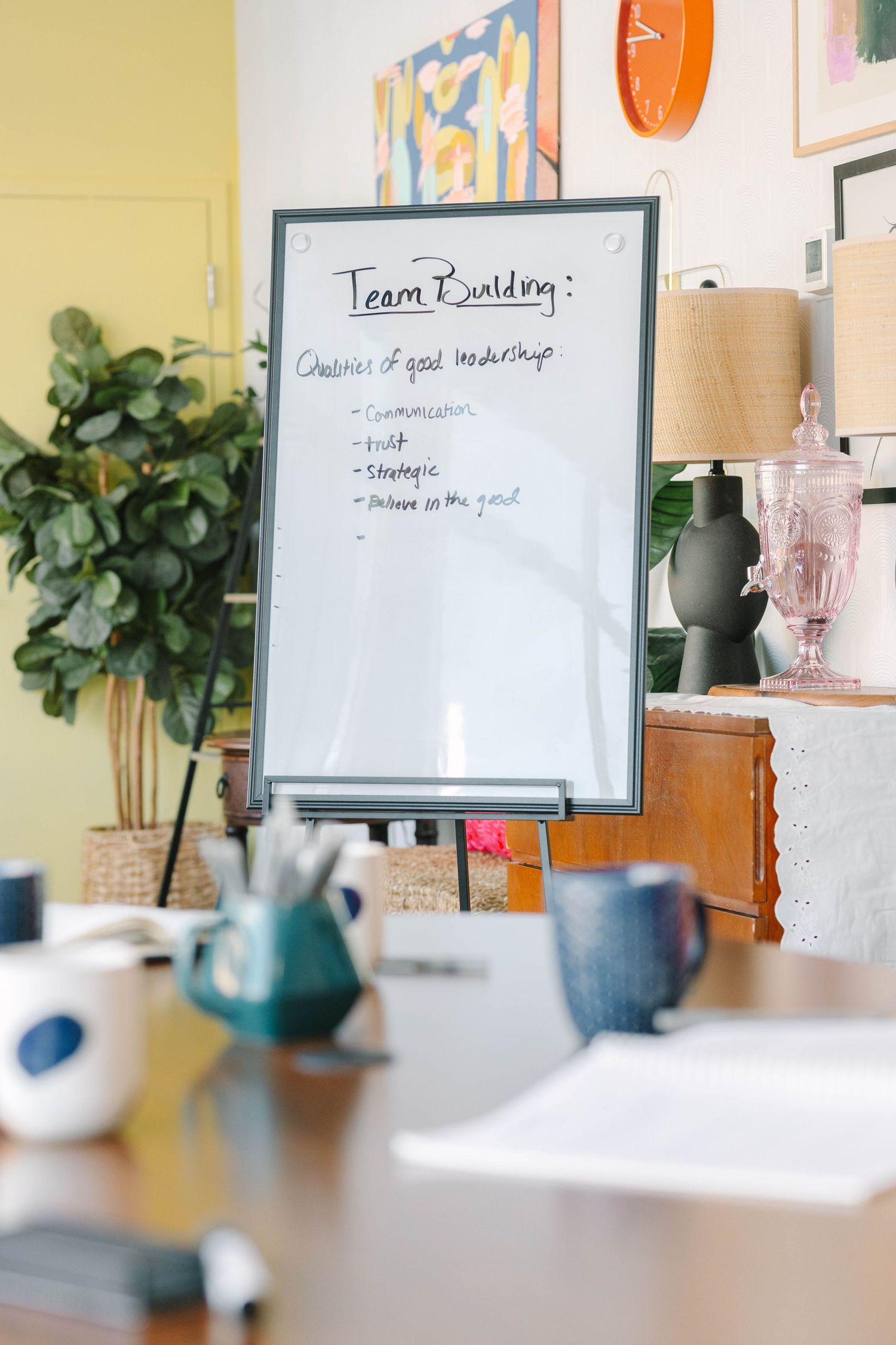 Whiteboard on easel displaying Team Building and qualities of good leadership in a cozy office meeting room.