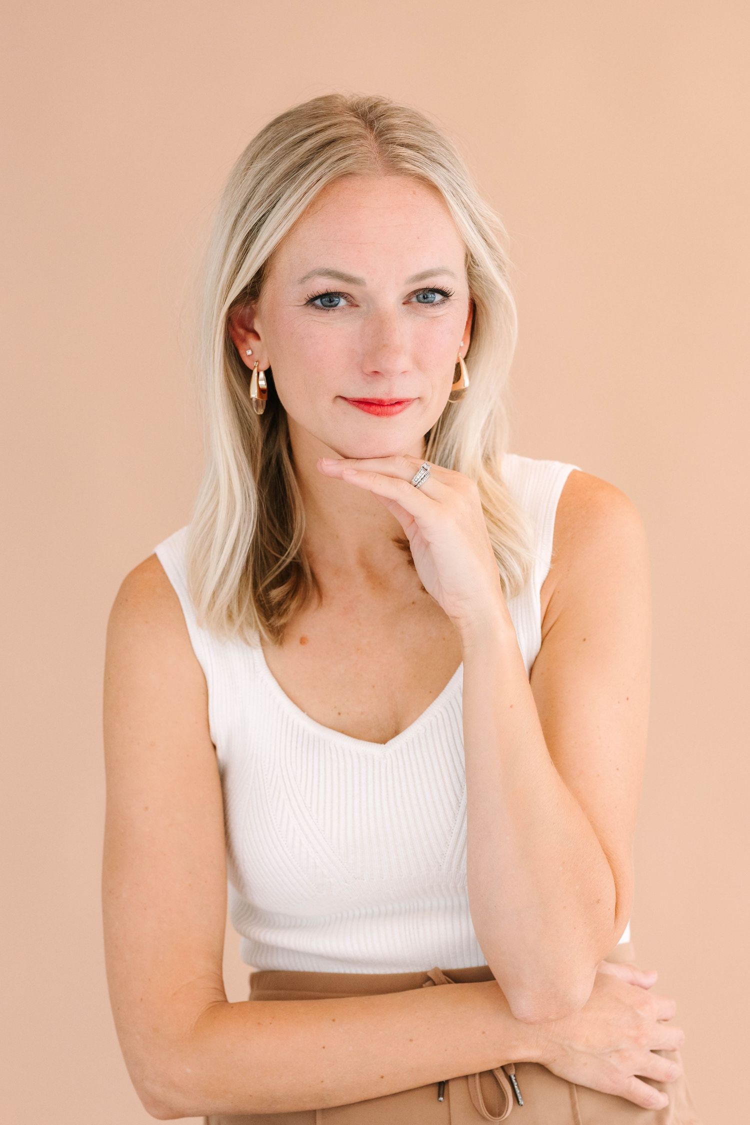 Portrait of person in white tank top against peach background with thoughtful expression.