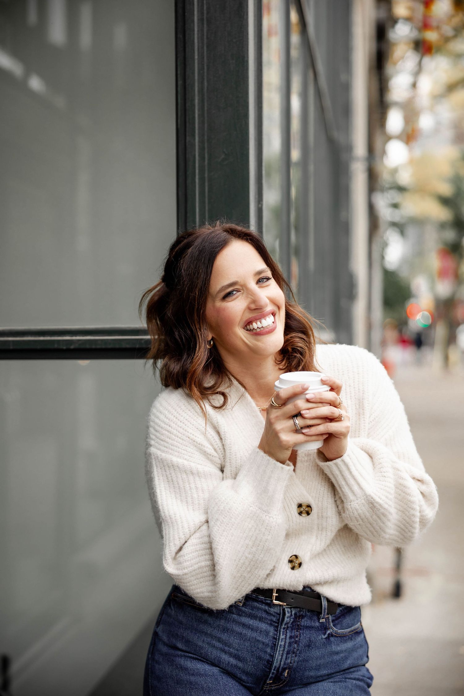 A candid series of photos showing someone in a white sweater and jeans laughing joyfully against an urban backdrop.