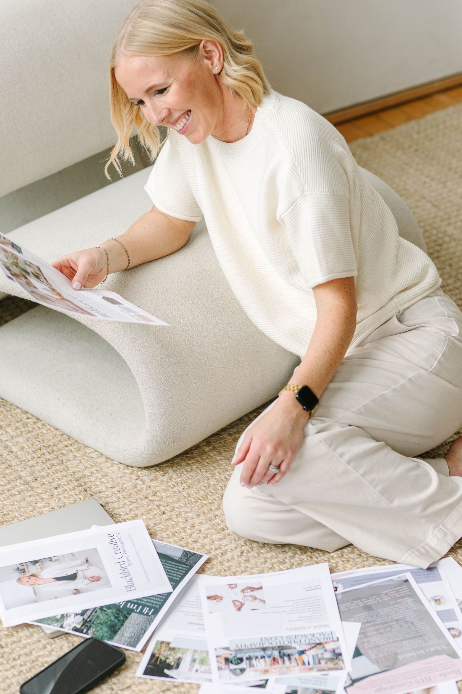 Person in white t-shirt and beige pants sits on floor looking through photo prints and memories.