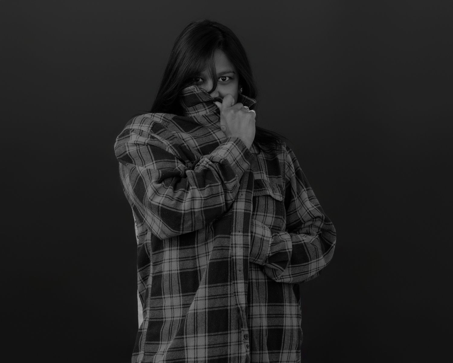 Black and white portrait of someone wearing a plaid button-up shirt in a dark studio setting.