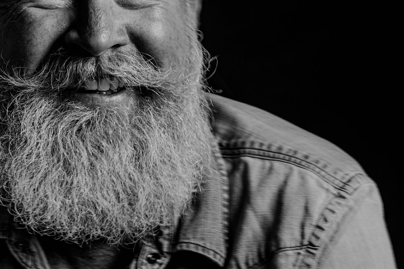 Side profile close-up of a grey beard and denim jacket in monochrome.