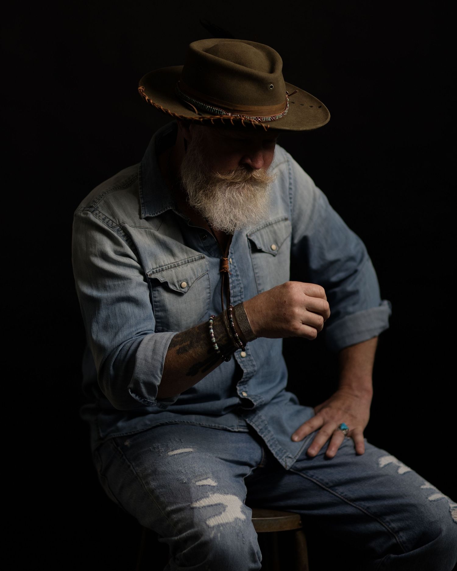 A figure in a denim jacket and cowboy hat sits in shadows taking a contemplative drag from a cigarette.
