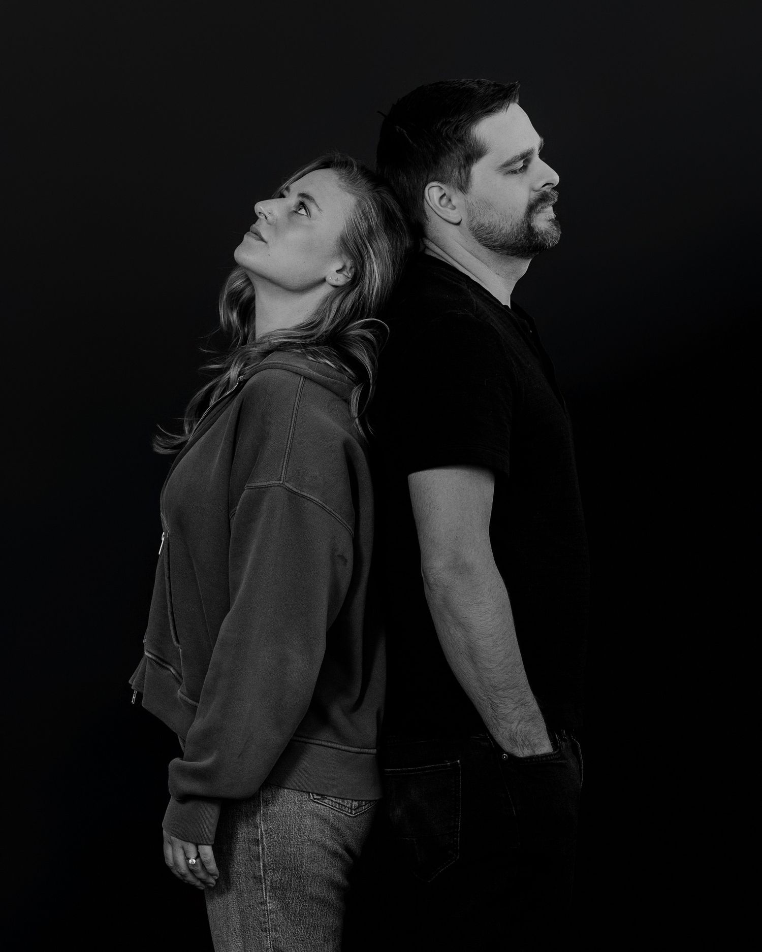 Dark moody portrait series showing couple in casual wear against black backdrop.