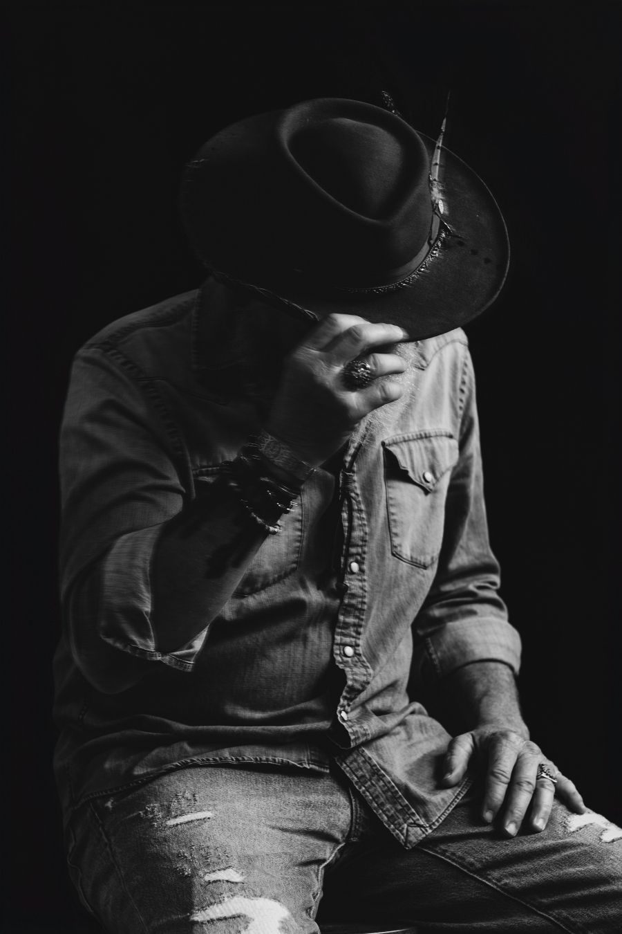Moody portrait showing figure in western hat with hand gesture against dark backdrop.