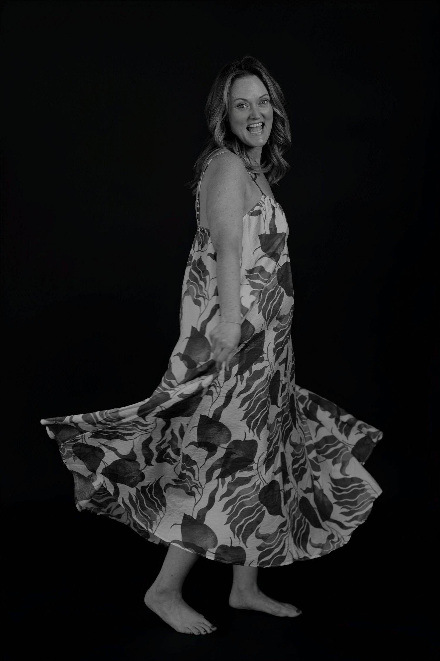 Dancing figure wearing flowing floral dress twirls against dark background in black and white.