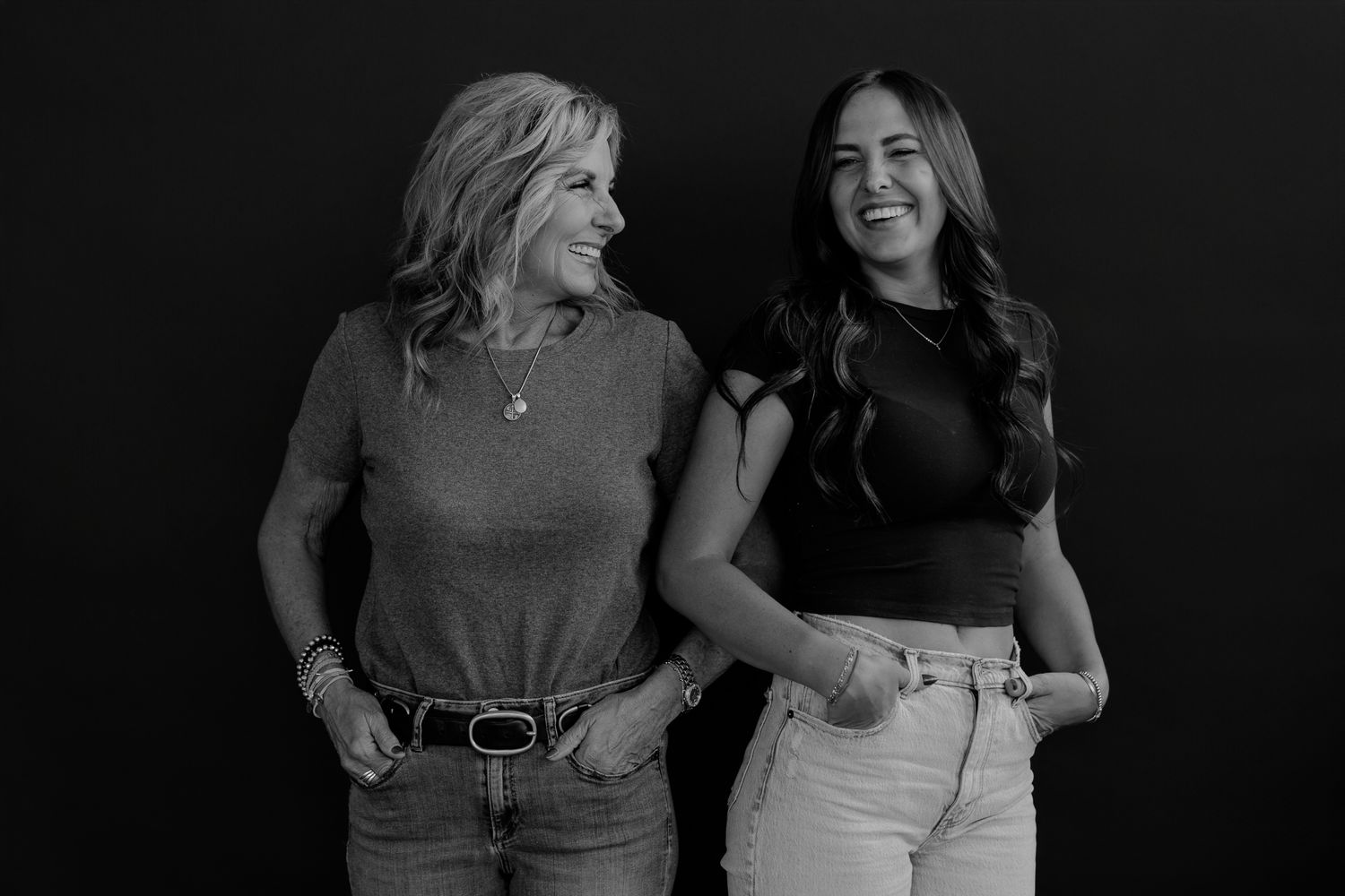 Black and white studio portrait captures genuine laughter between two women in casual attire.