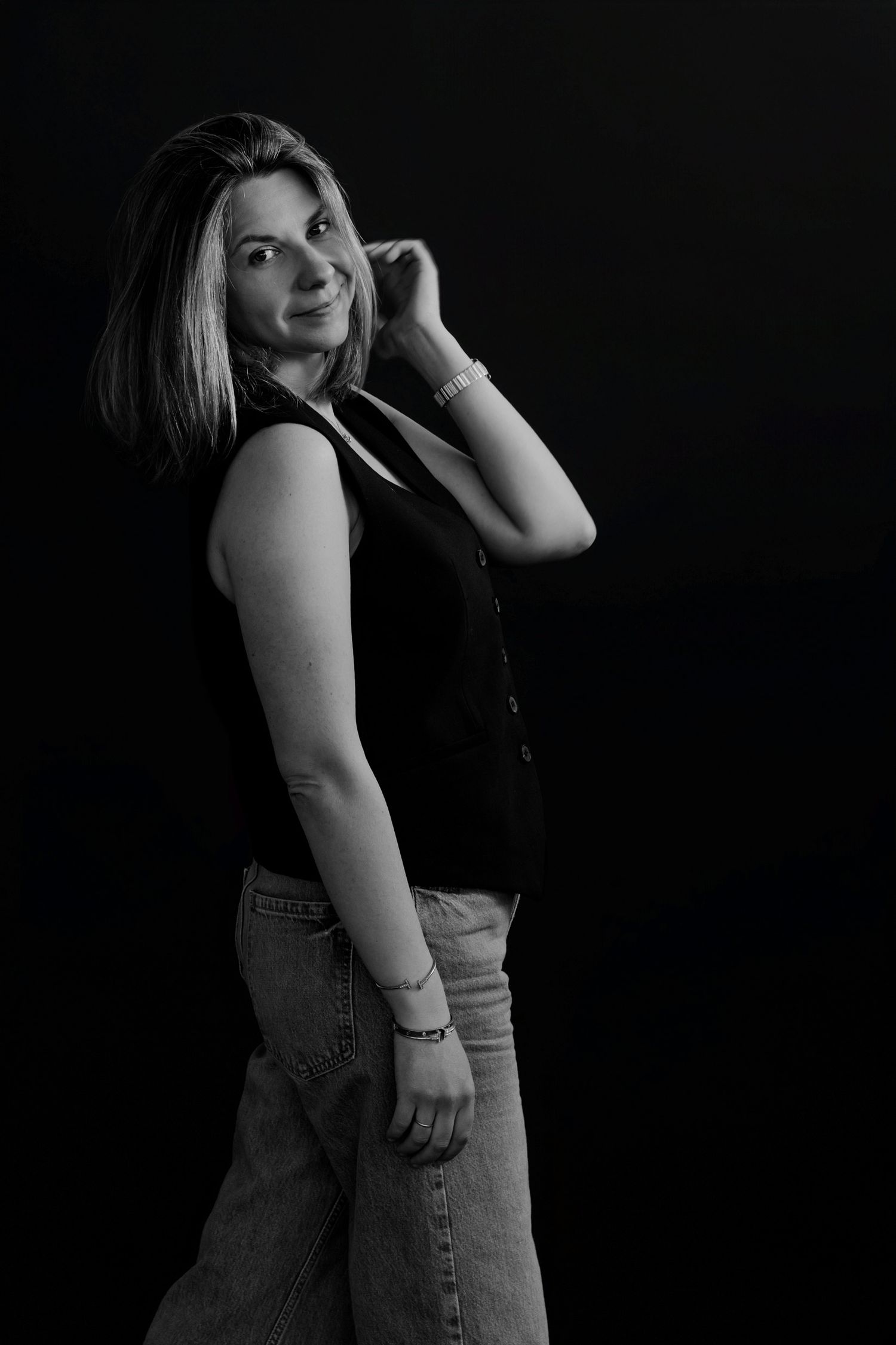 Casual portrait series with person in dark top and jeans against black backdrop.