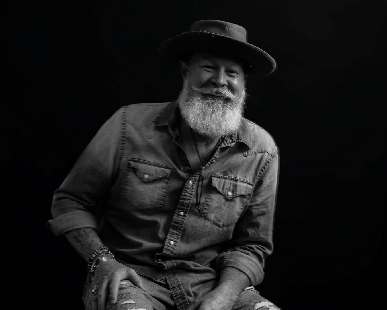 Low-key portrait showing relaxed pose in western hat and denim shirt.