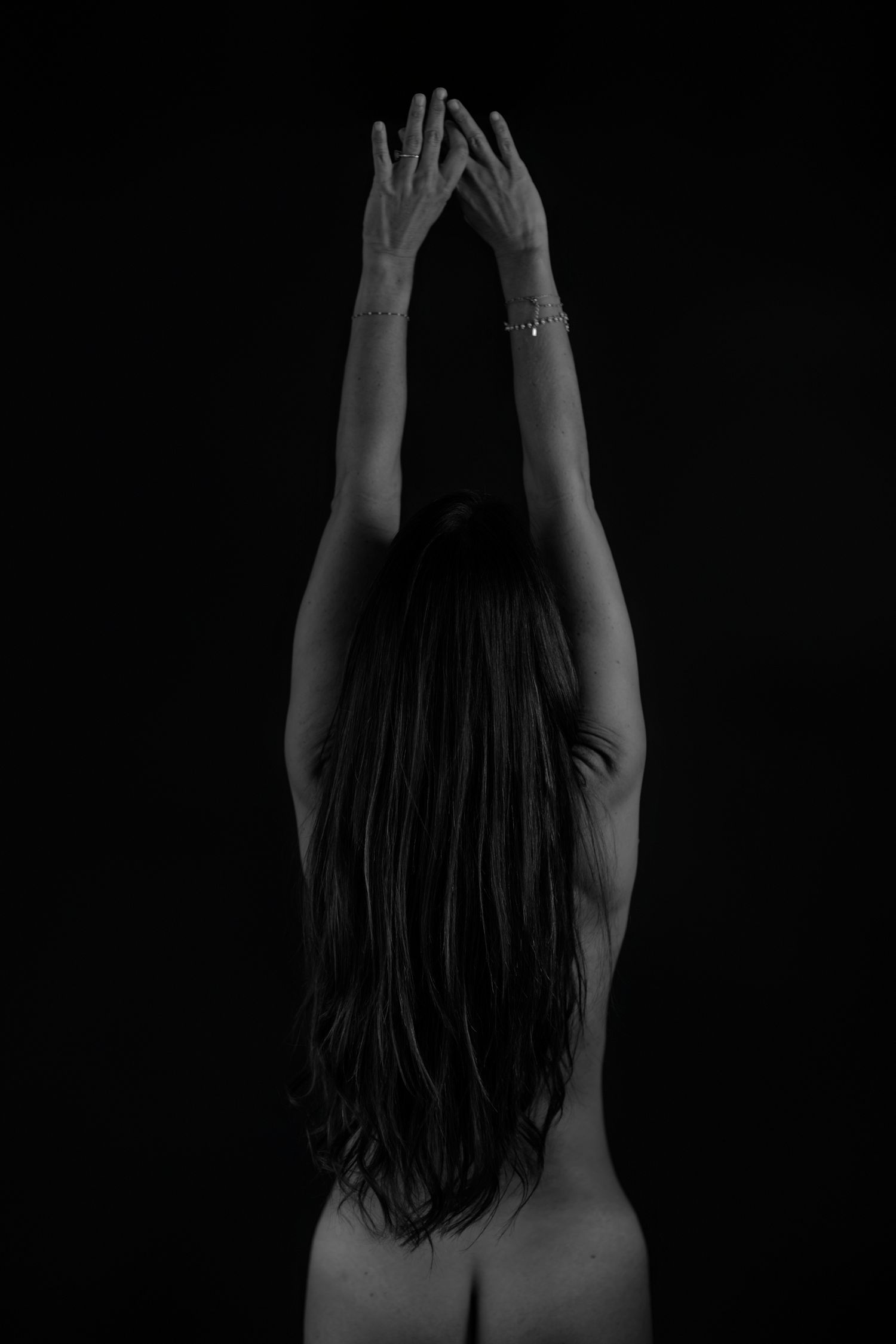 Black and white artistic portrait showing figure with long dark hair against dark background in dramatic lighting.