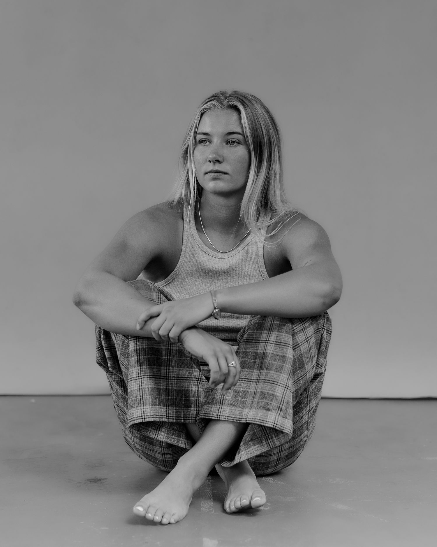 Figure in tank top and plaid pants sits in contemplative poses against gray background.
