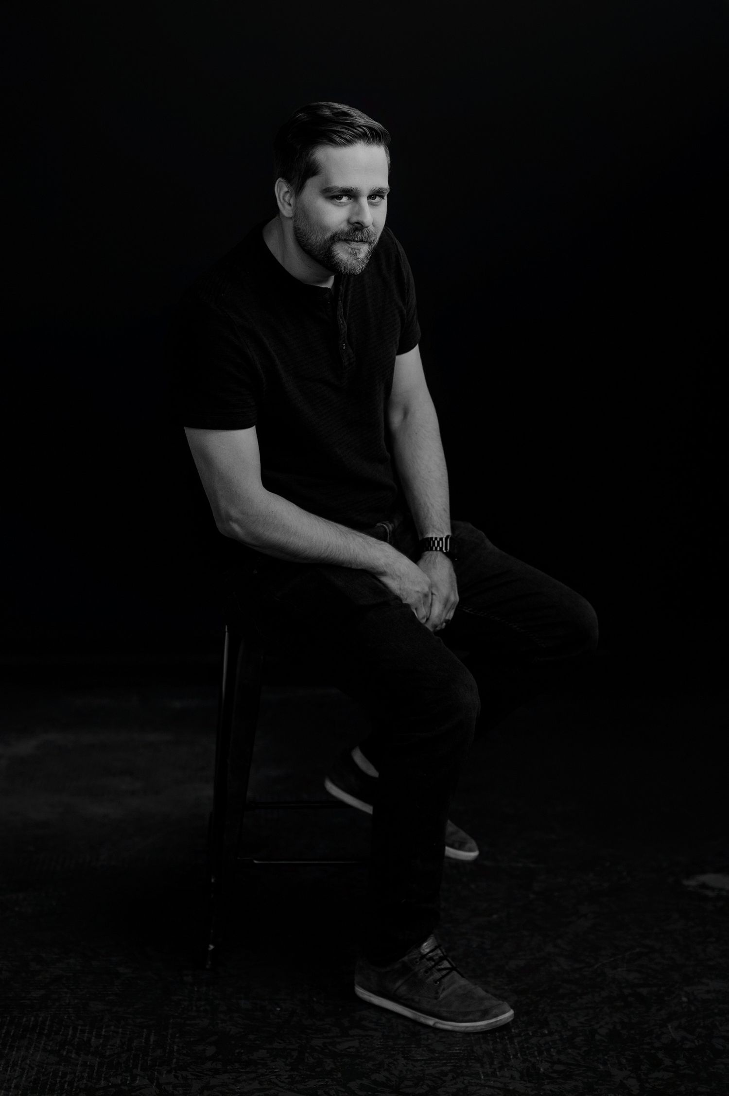 Moody studio portraits of person in black shirt seated against dark background.