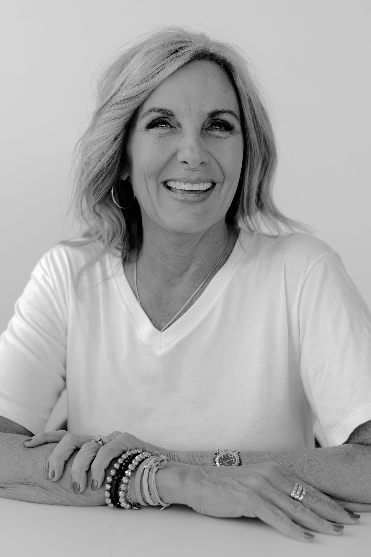 Black and white photo sequence showing relaxed poses in white v-neck top with bracelets.
