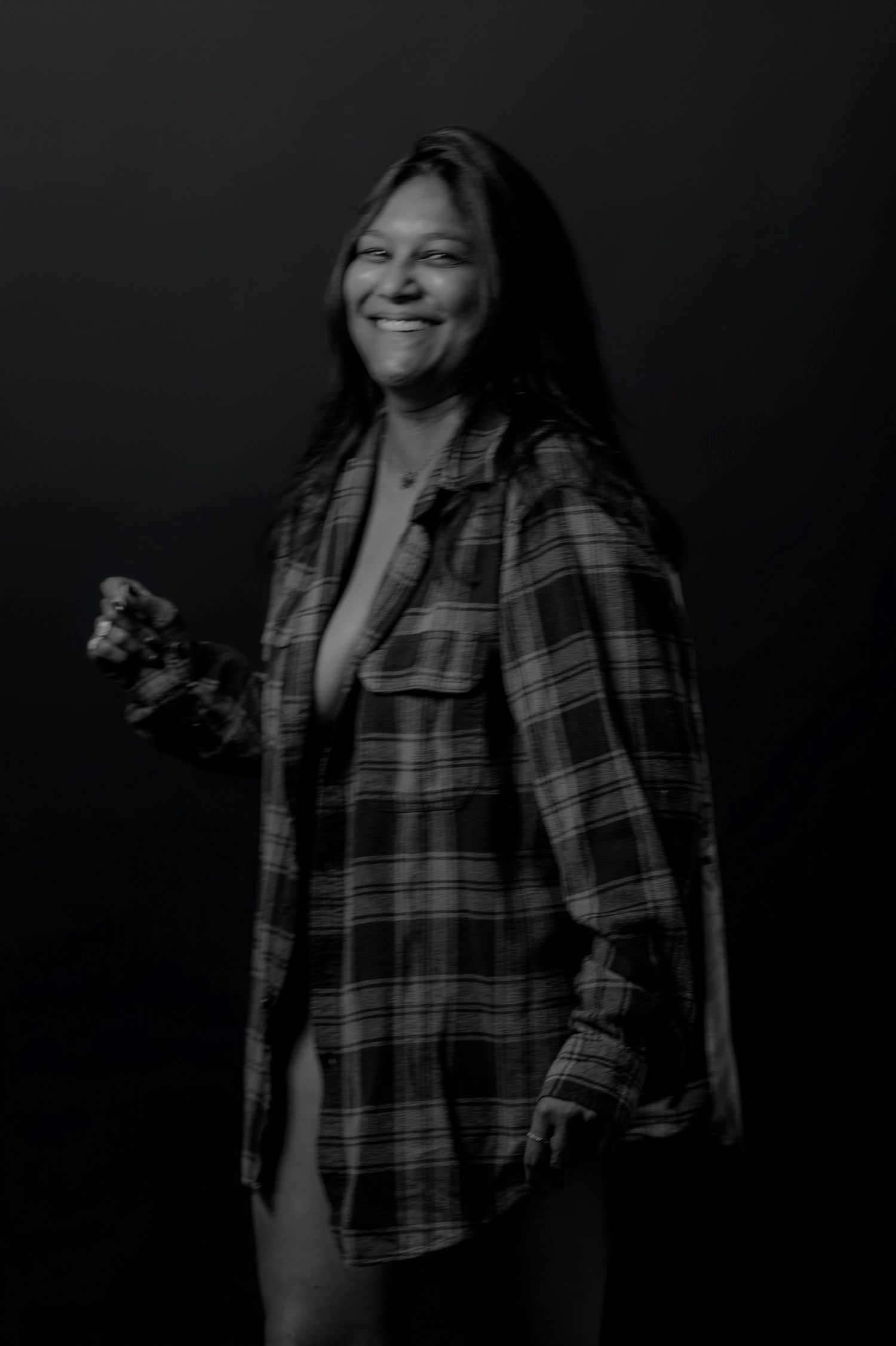 Casual studio portrait showing relaxed pose in plaid shirt against black backdrop.