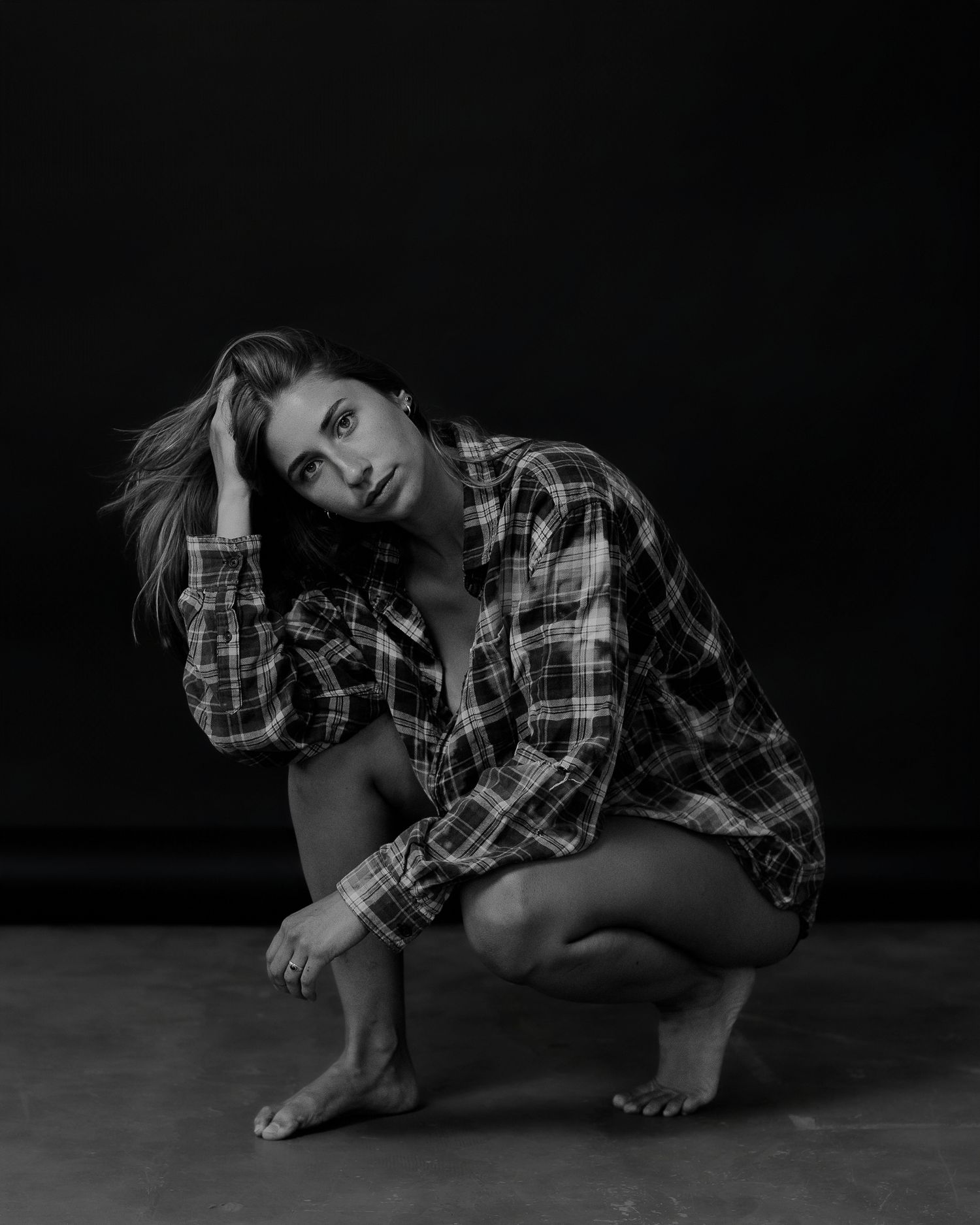 Person in plaid shirt poses dramatically on floor in dark monochrome series.