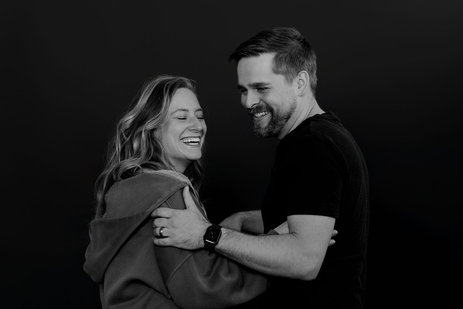 Candid studio shot of couple sharing genuine laughter while embracing.