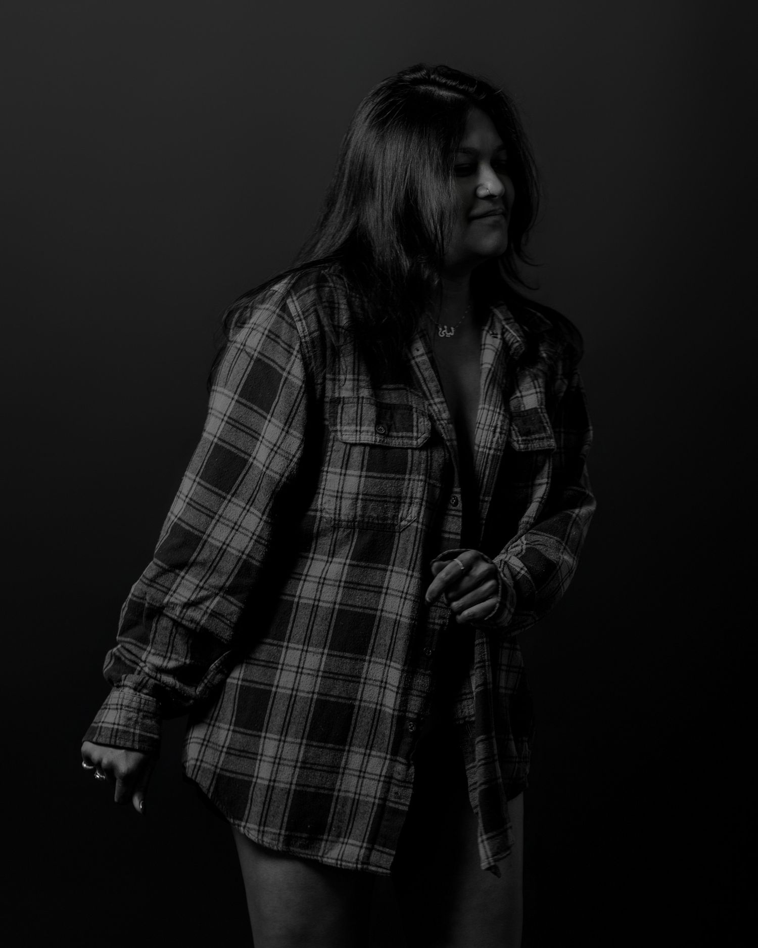 Figure in plaid shirt poses against dark background in moody black and white photography.