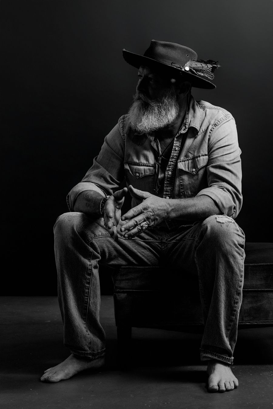 Moody black and white shots of figure in hat sitting barefoot on dark surface.