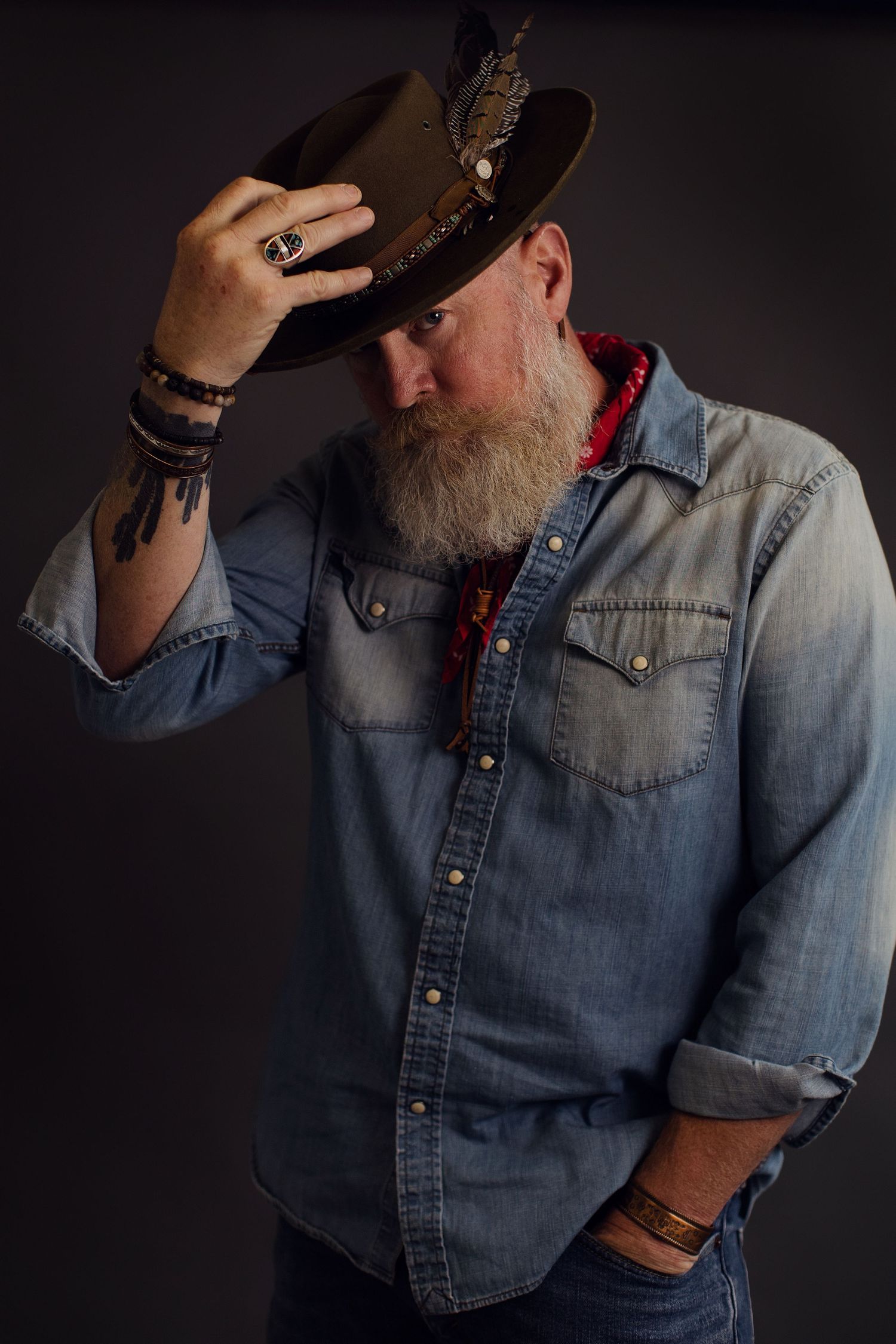 A series of moody portraits showing someone in denim western shirt against dark background tilting black cowboy hat.