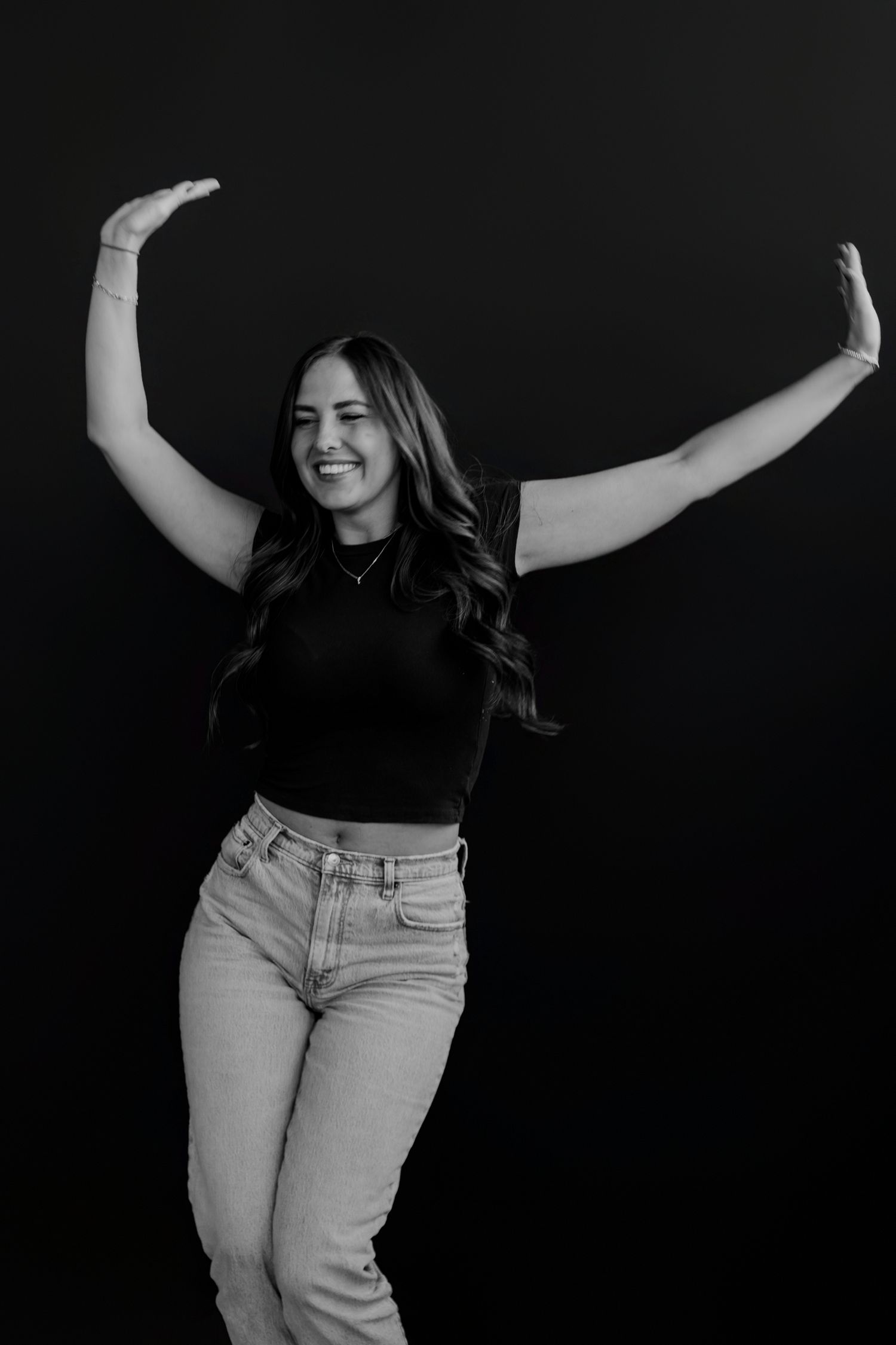 Energetic dance pose with arms raised captured in monochrome studio setting.