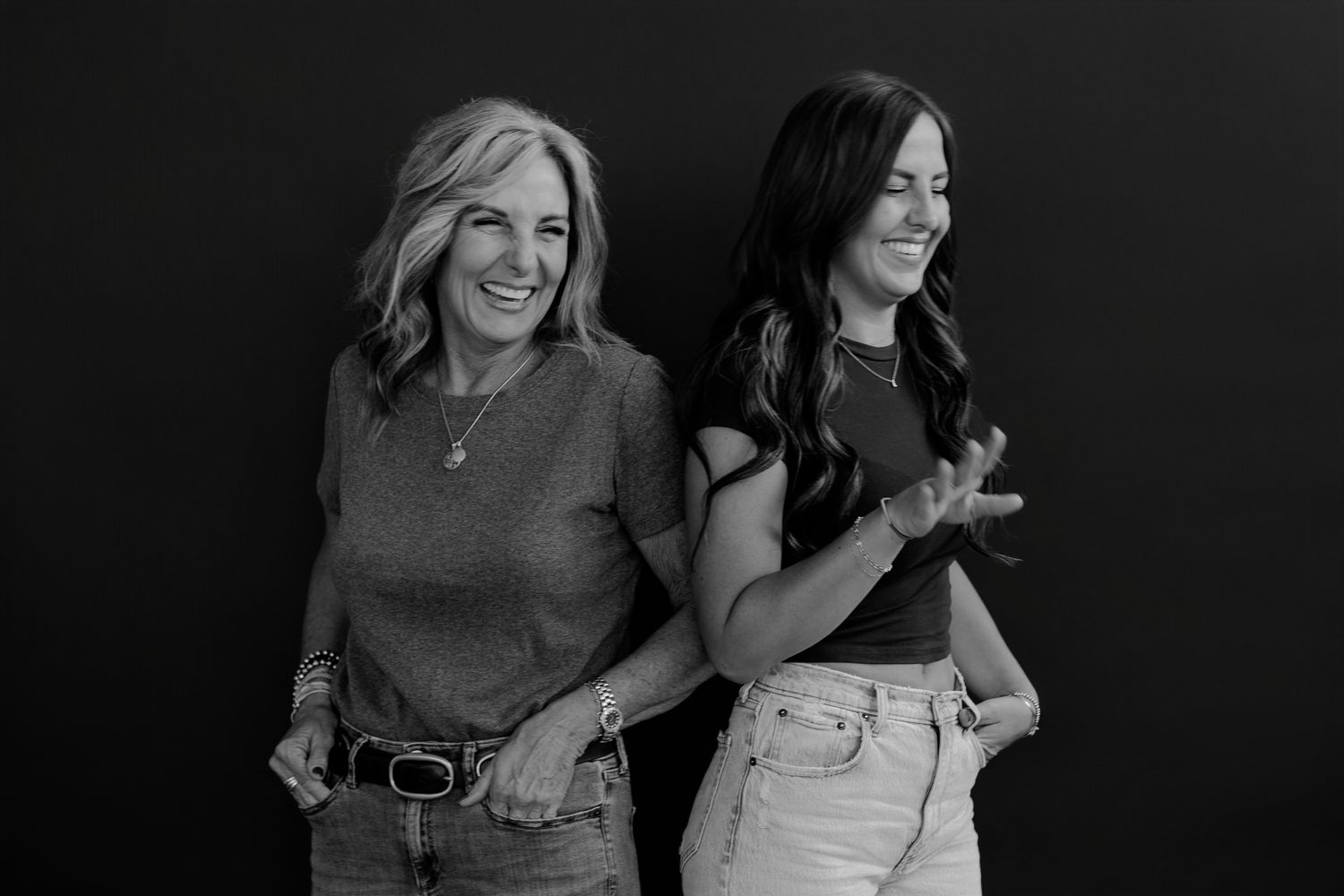 Two women display genuine happiness in casual black and white studio photograph.