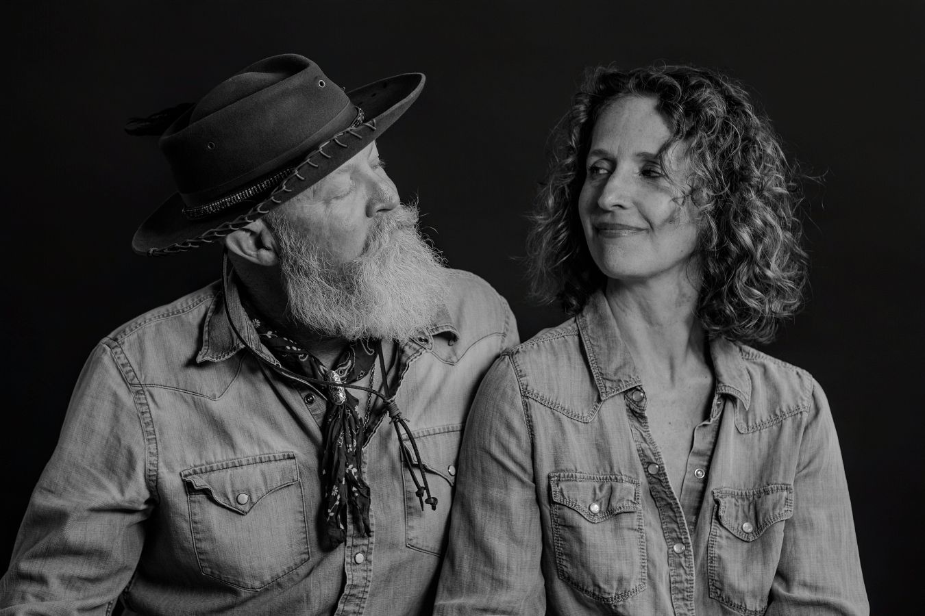 Couple in denim jackets share intimate moment in dramatic black and white portrait.