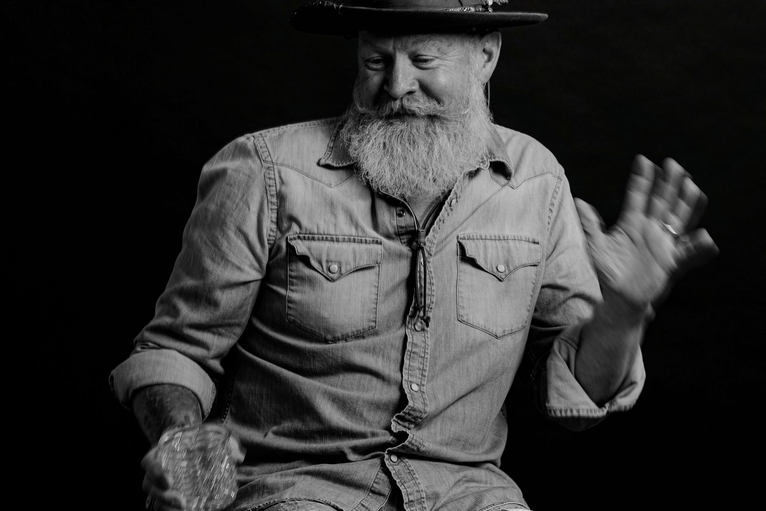 Dramatic black and white portraits of a bearded person in denim gesturing expressively.
