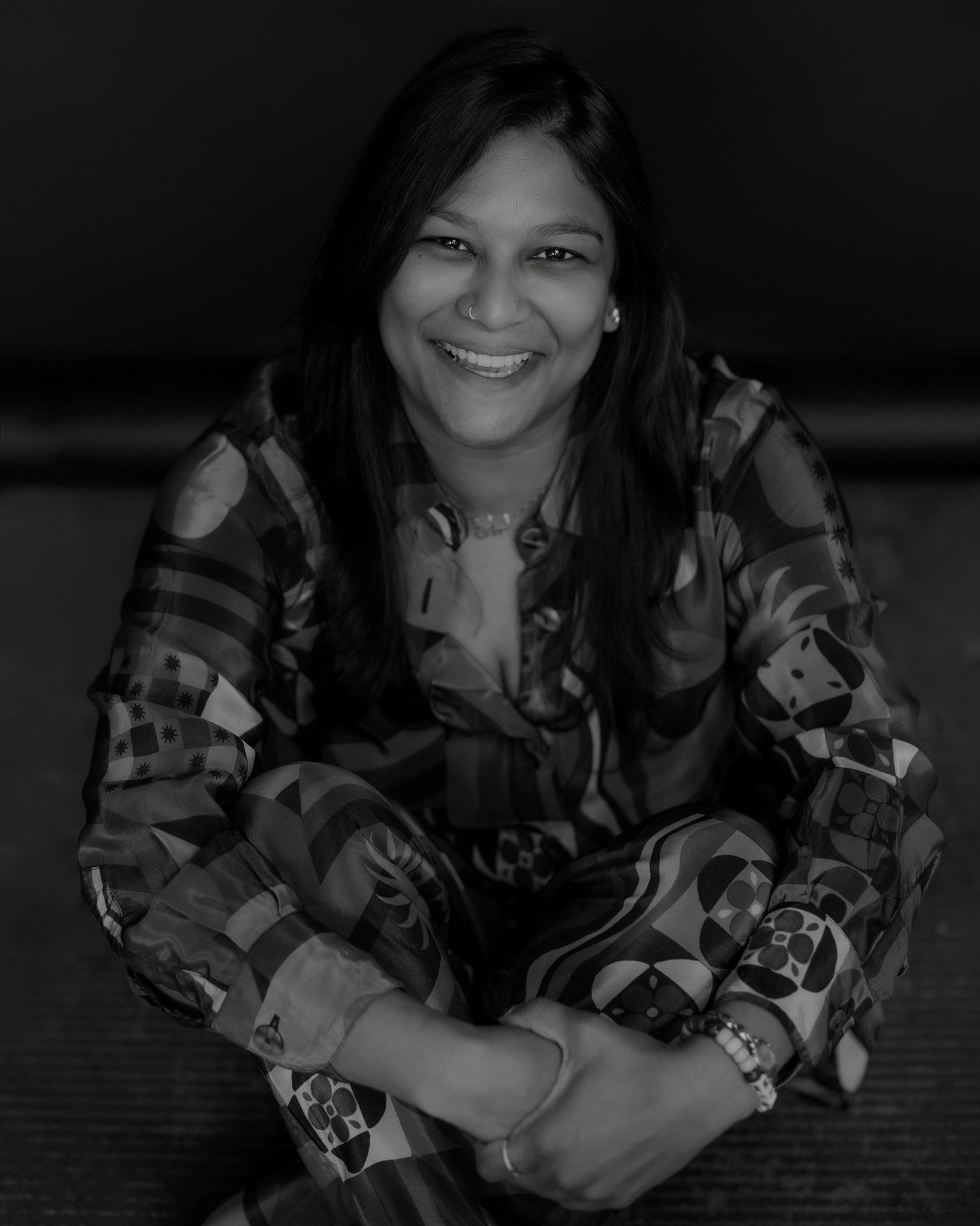 Person smiling and posing playfully in floral print clothing against dark backdrop.